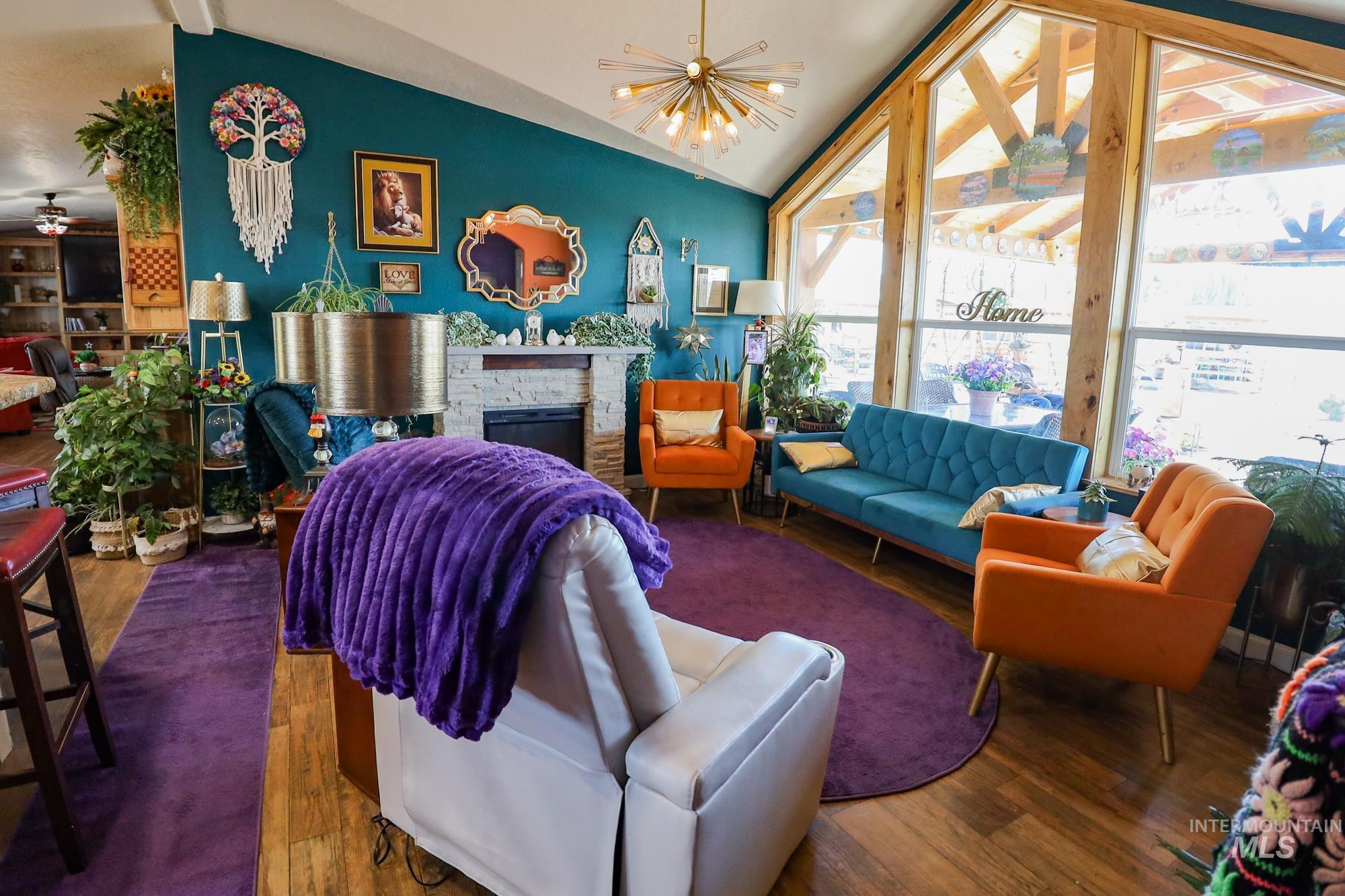 Living room featuring vaulted ceiling, wood finished floors, and a stone fireplace