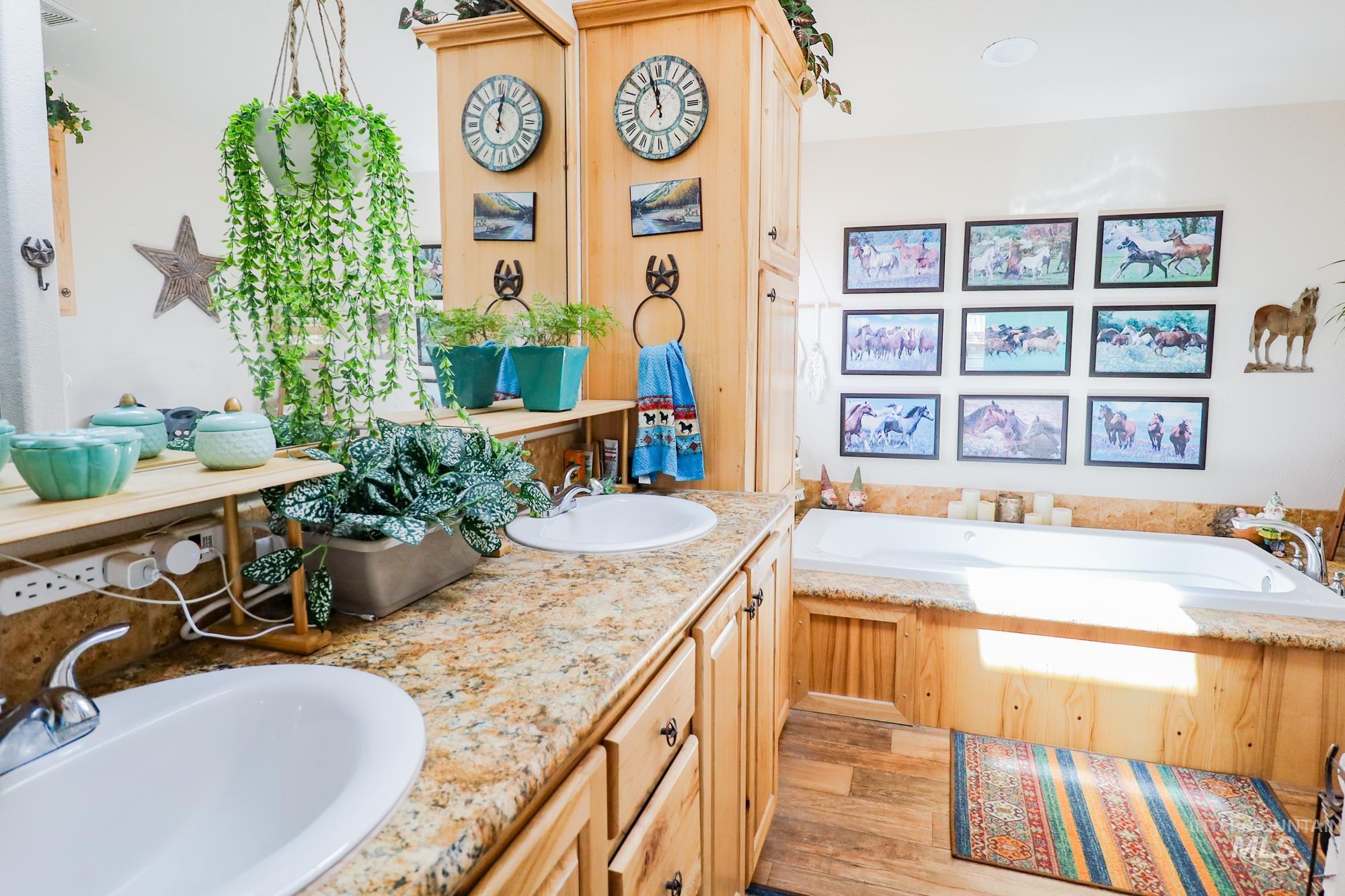 Full bathroom with double vanity, a garden tub, and wood finished floors