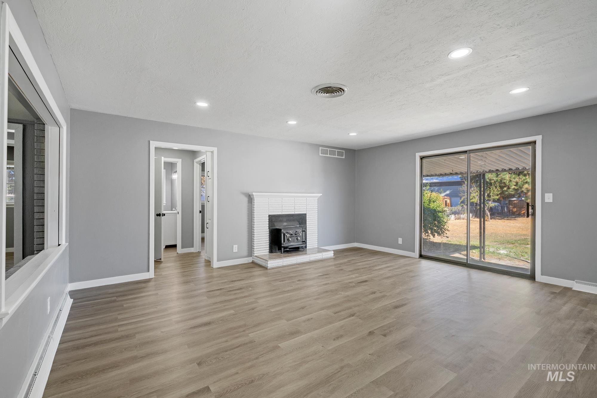 Unfurnished living room featuring recessed lighting, light wood finished floors, a textured ceiling, a wood stove, and a baseboard heating unit