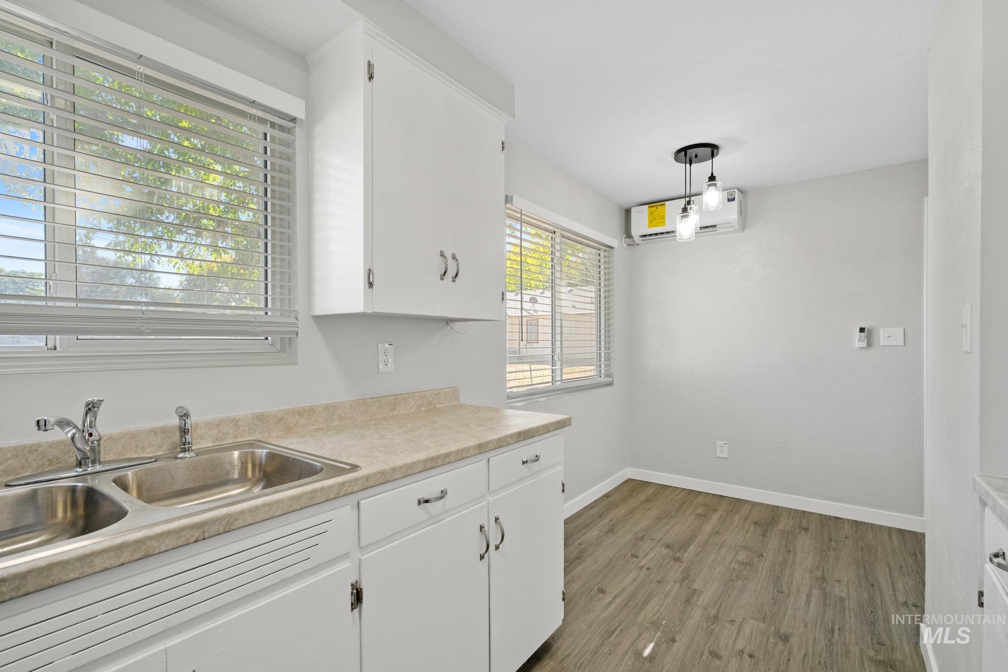Kitchen featuring light countertops, white cabinets, a wall unit AC, wood finished floors, and pendant lighting