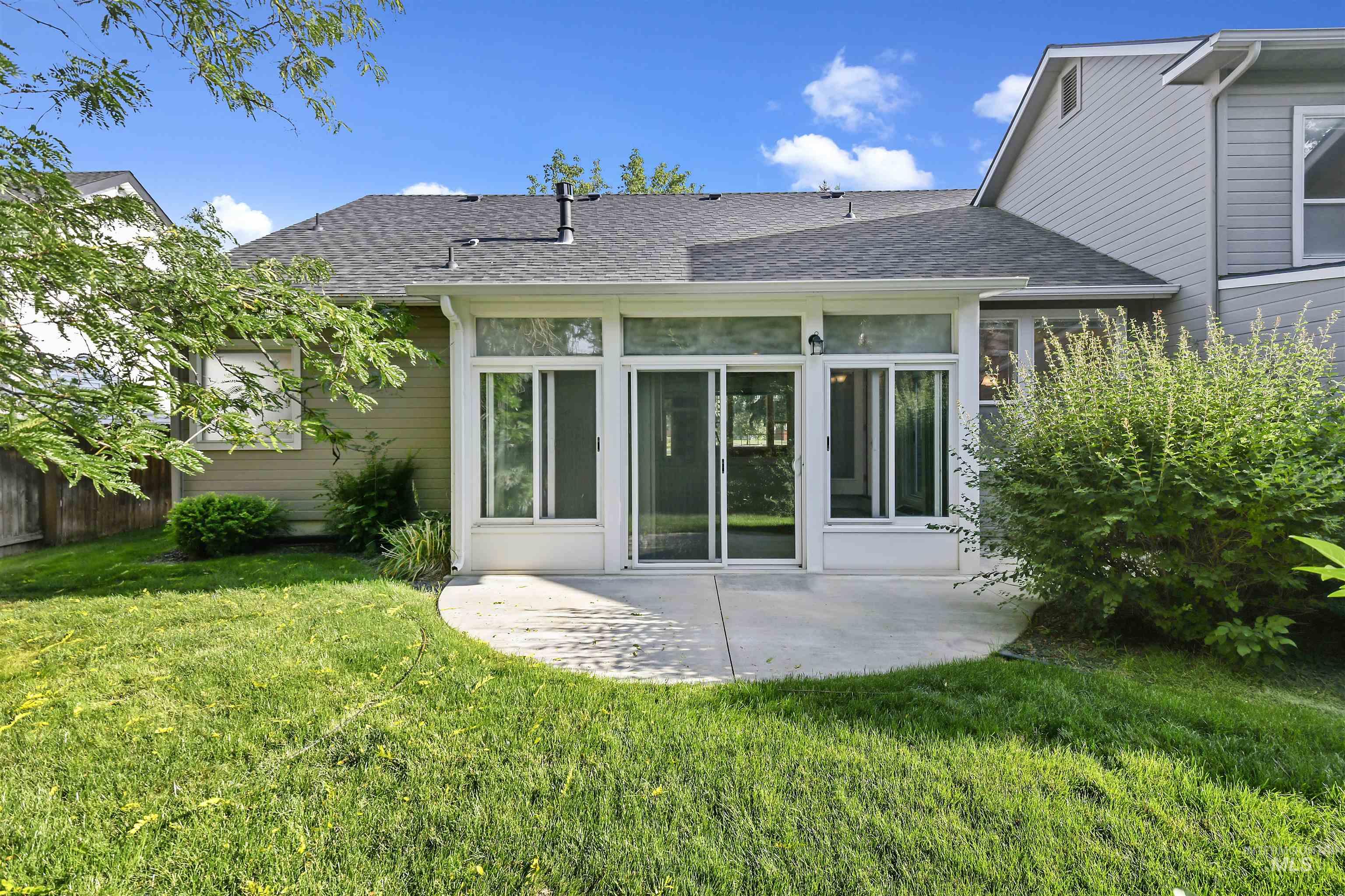 Rear view of property featuring a shingled roof, a patio area, and a sunroom