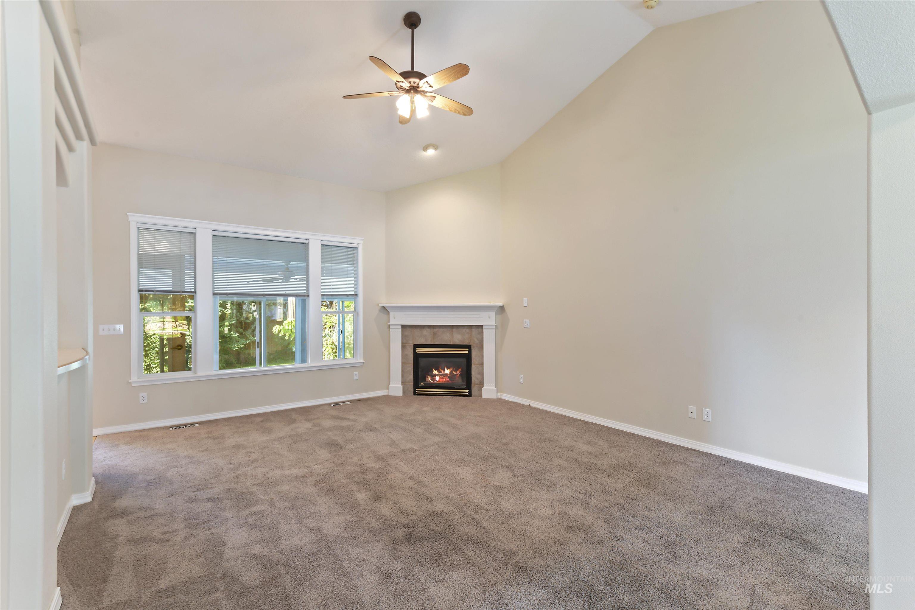 Unfurnished living room with carpet floors, a ceiling fan, a fireplace, and high vaulted ceiling