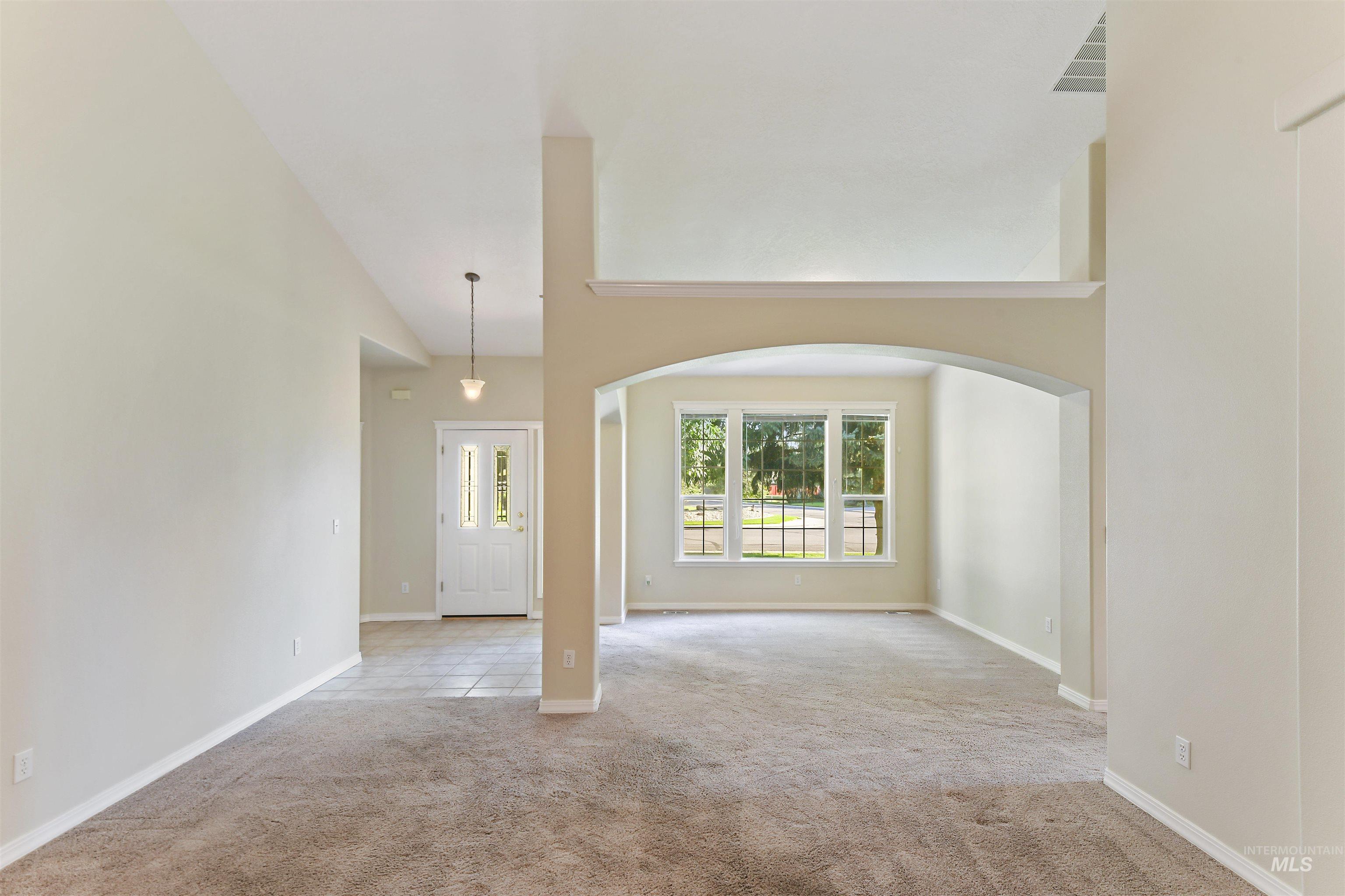 Unfurnished room featuring arched walkways, light colored carpet, and a high ceiling