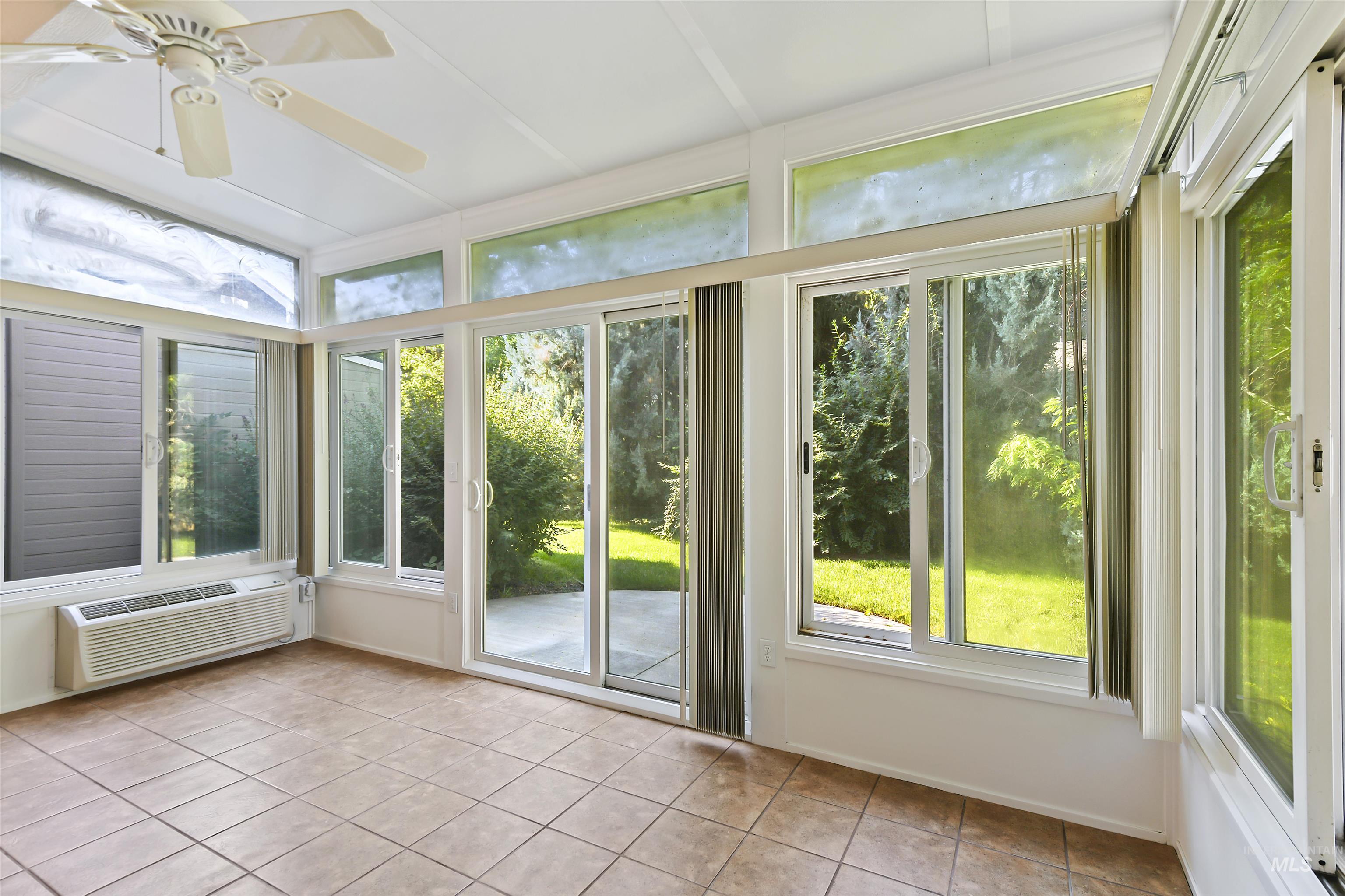 Unfurnished sunroom featuring tile patterned flooring, a wall mounted air conditioner, and ceiling fan