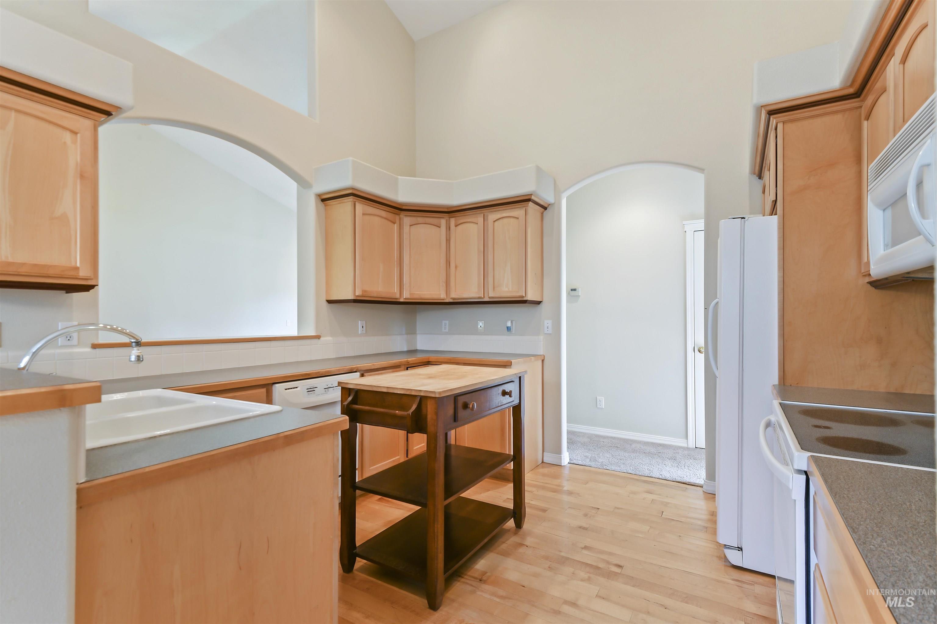 Kitchen featuring white appliances, light brown cabinetry, light wood finished floors, arched walkways, and a high ceiling