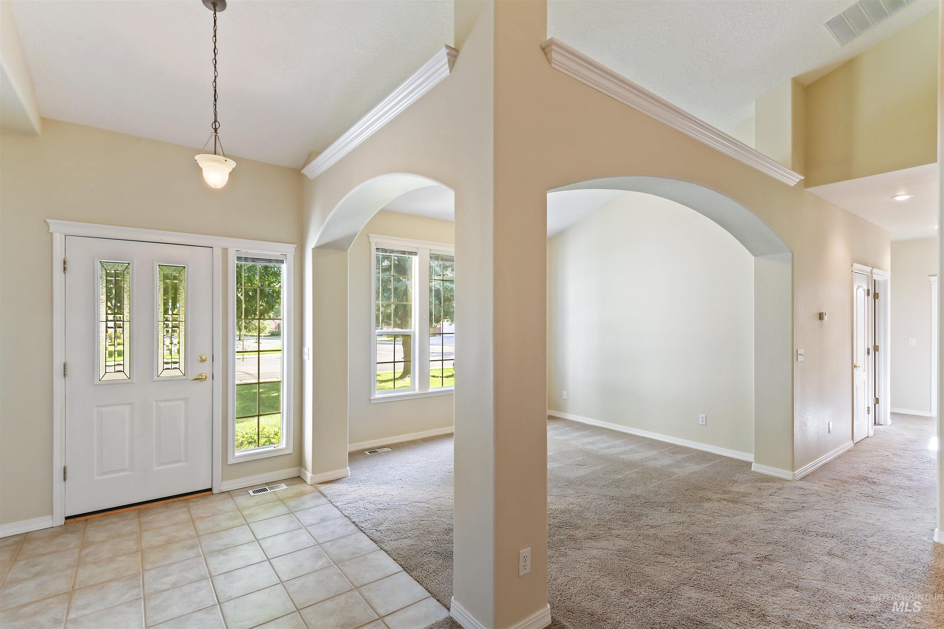 Foyer entrance featuring arched walkways, light tile patterned floors, light carpet, and crown molding