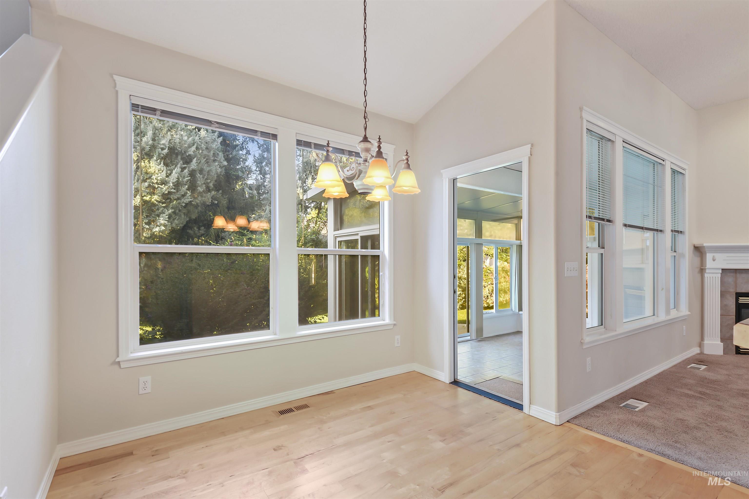 Unfurnished dining area with healthy amount of natural light, a chandelier, light wood-style floors, a fireplace, and lofted ceiling