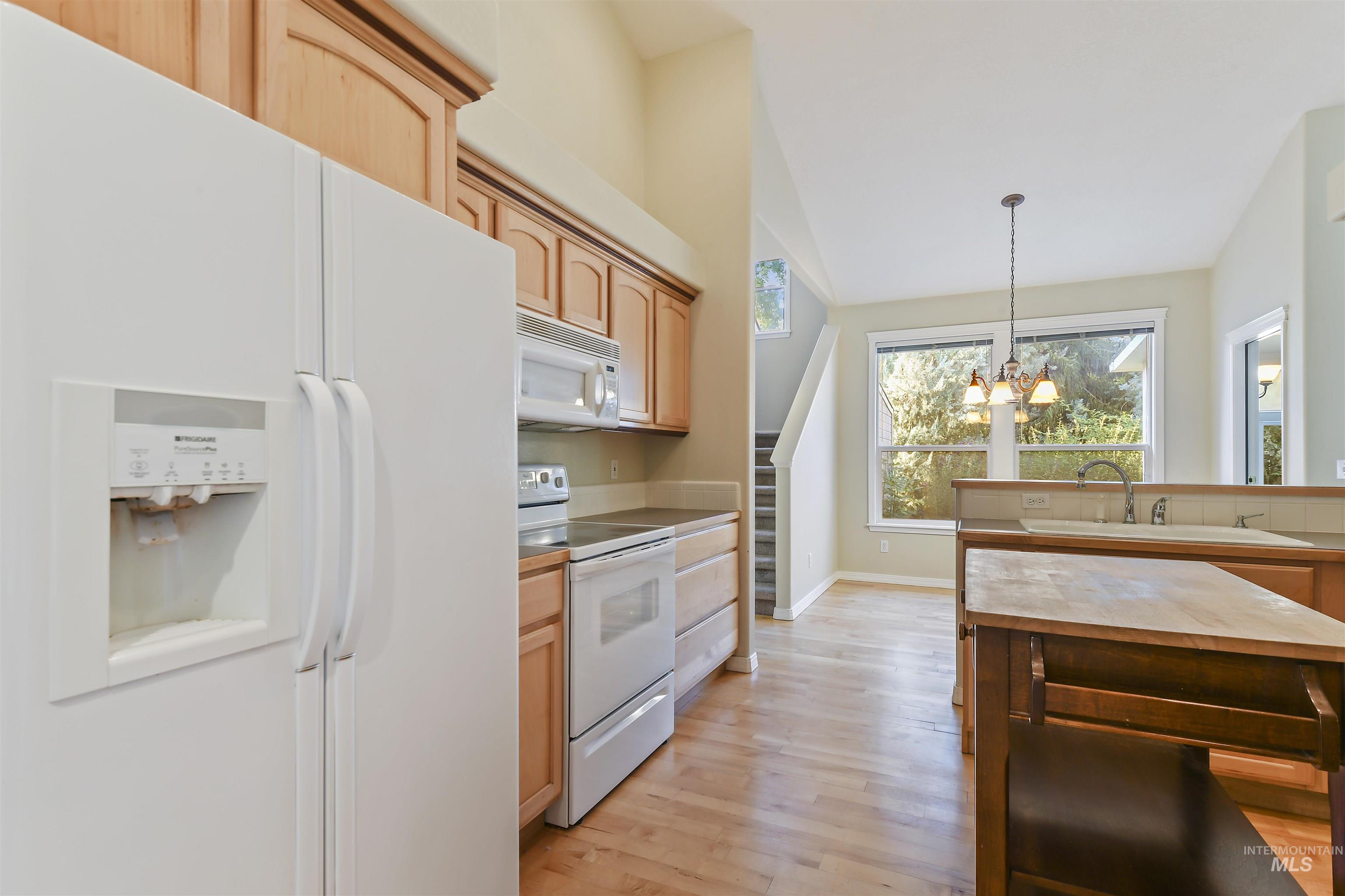 Kitchen featuring white appliances, hanging light fixtures, a chandelier, light wood-style flooring, and light countertops