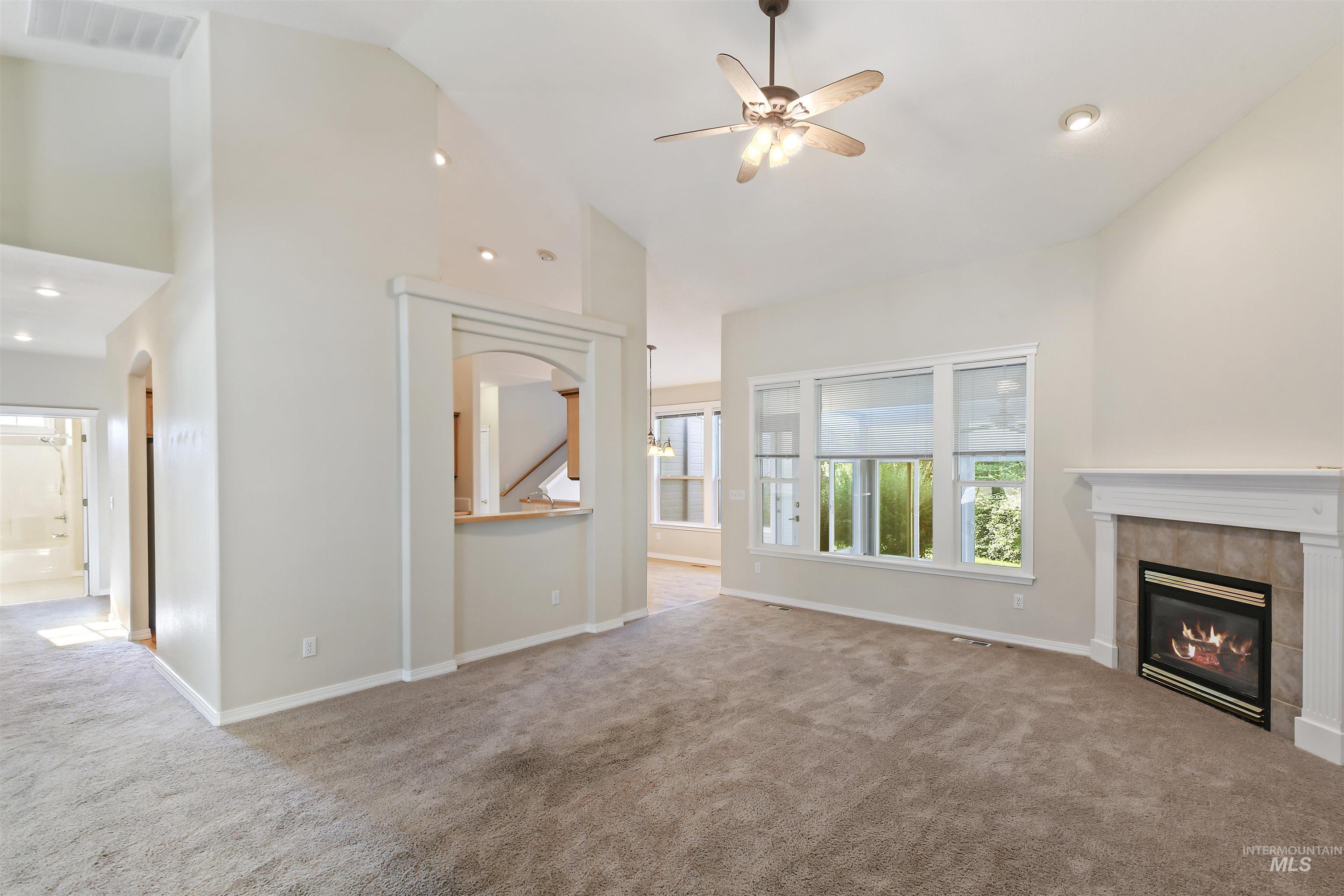 Unfurnished living room with high vaulted ceiling, carpet floors, a tiled fireplace, ceiling fan, and recessed lighting