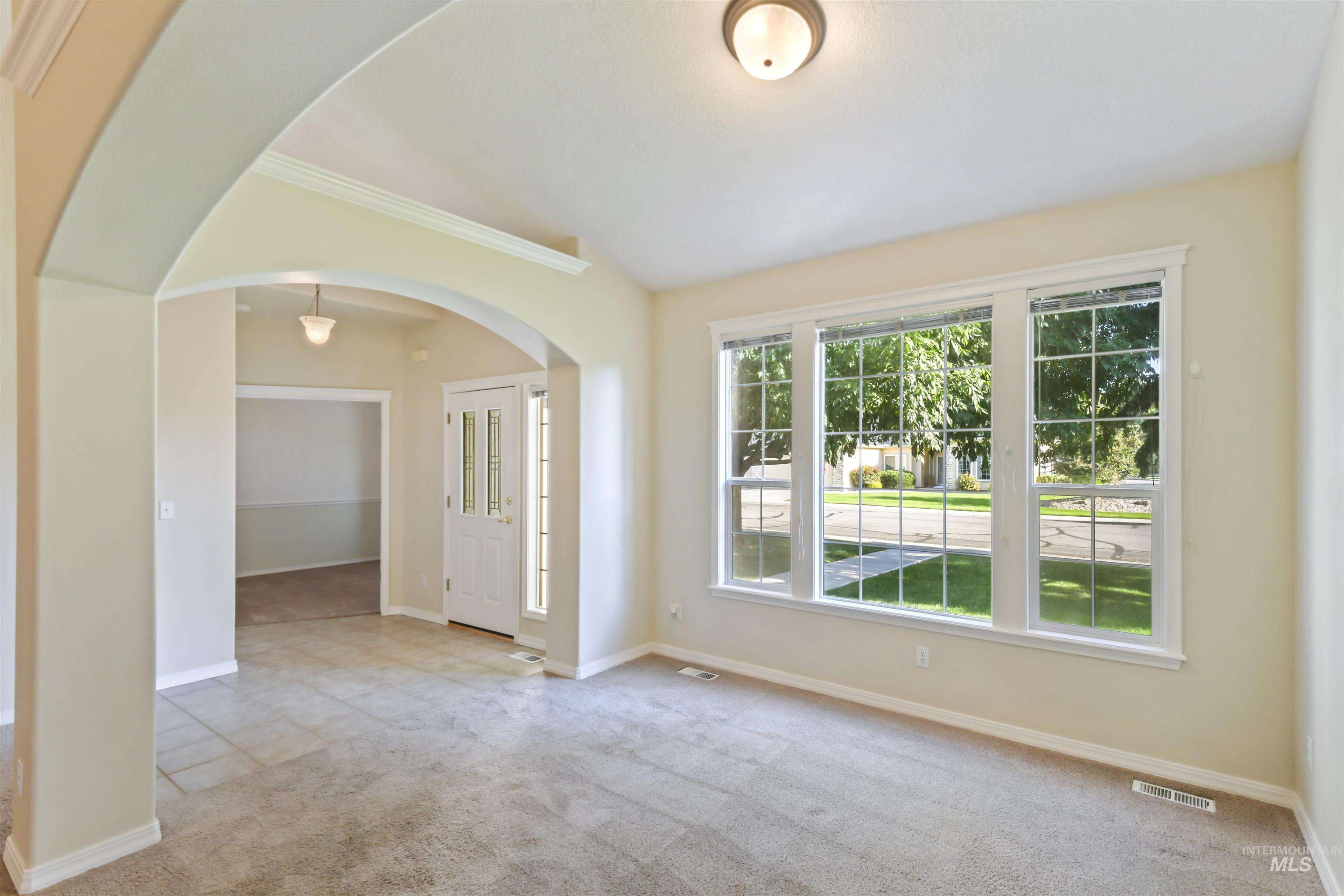 Empty room featuring light colored carpet, arched walkways, crown molding, and light tile patterned floors
