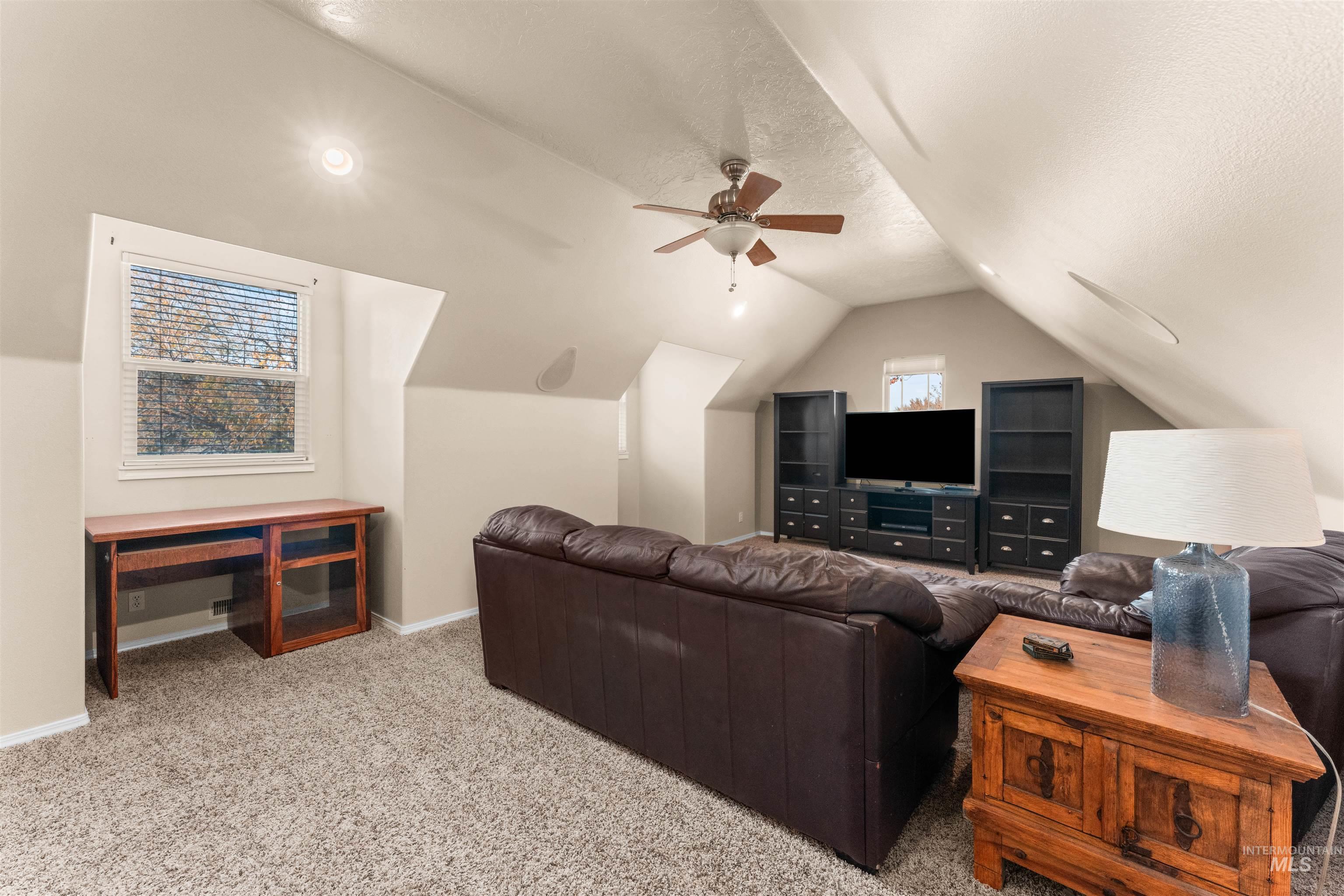 Living room with light colored carpet, a textured ceiling, plenty of natural light, lofted ceiling, and ceiling fan