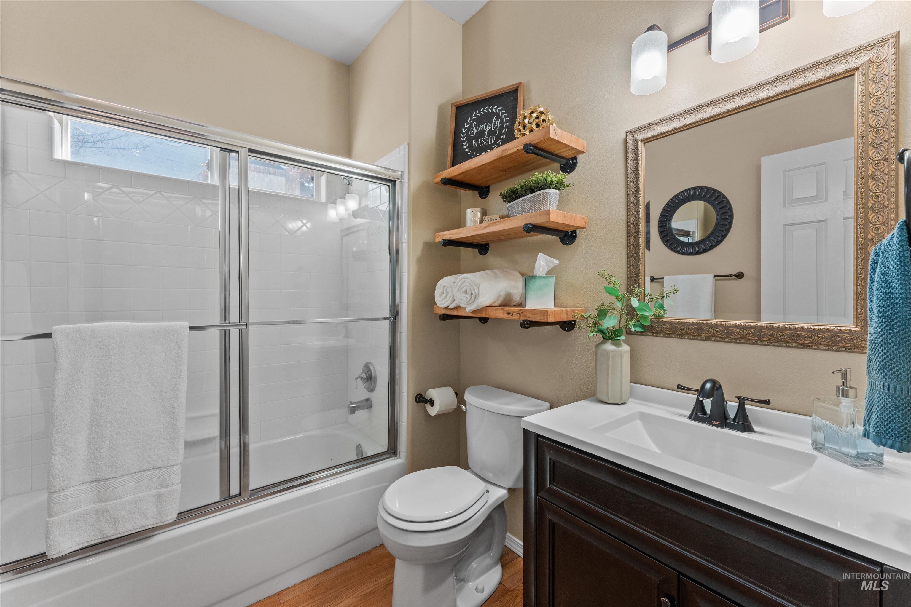 Full bath featuring vanity, combined bath / shower with glass door, and light wood finished floors