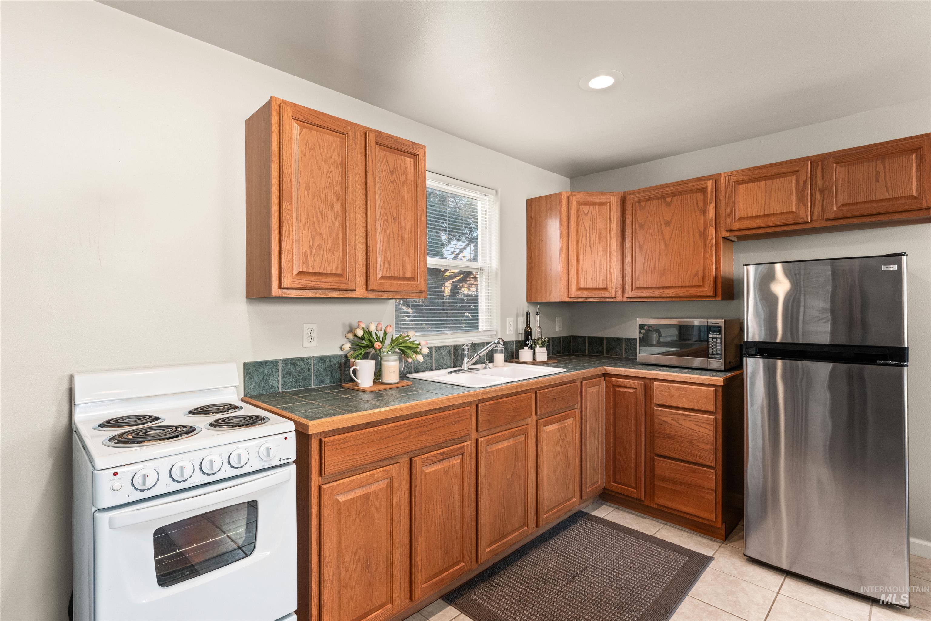 Kitchen with appliances with stainless steel finishes, brown cabinets, light tile patterned flooring, and recessed lighting