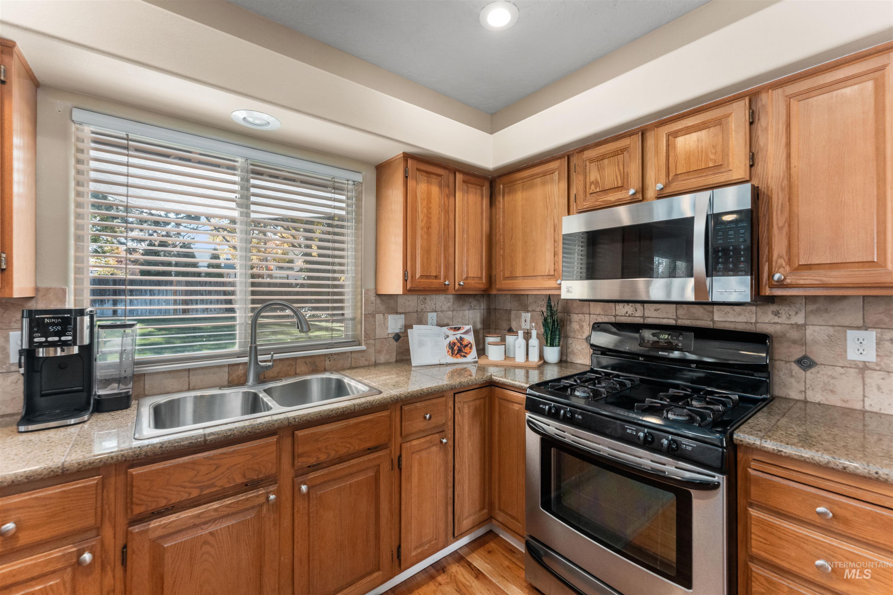 Kitchen with stainless steel appliances, brown cabinetry, backsplash, light wood-style floors, and recessed lighting