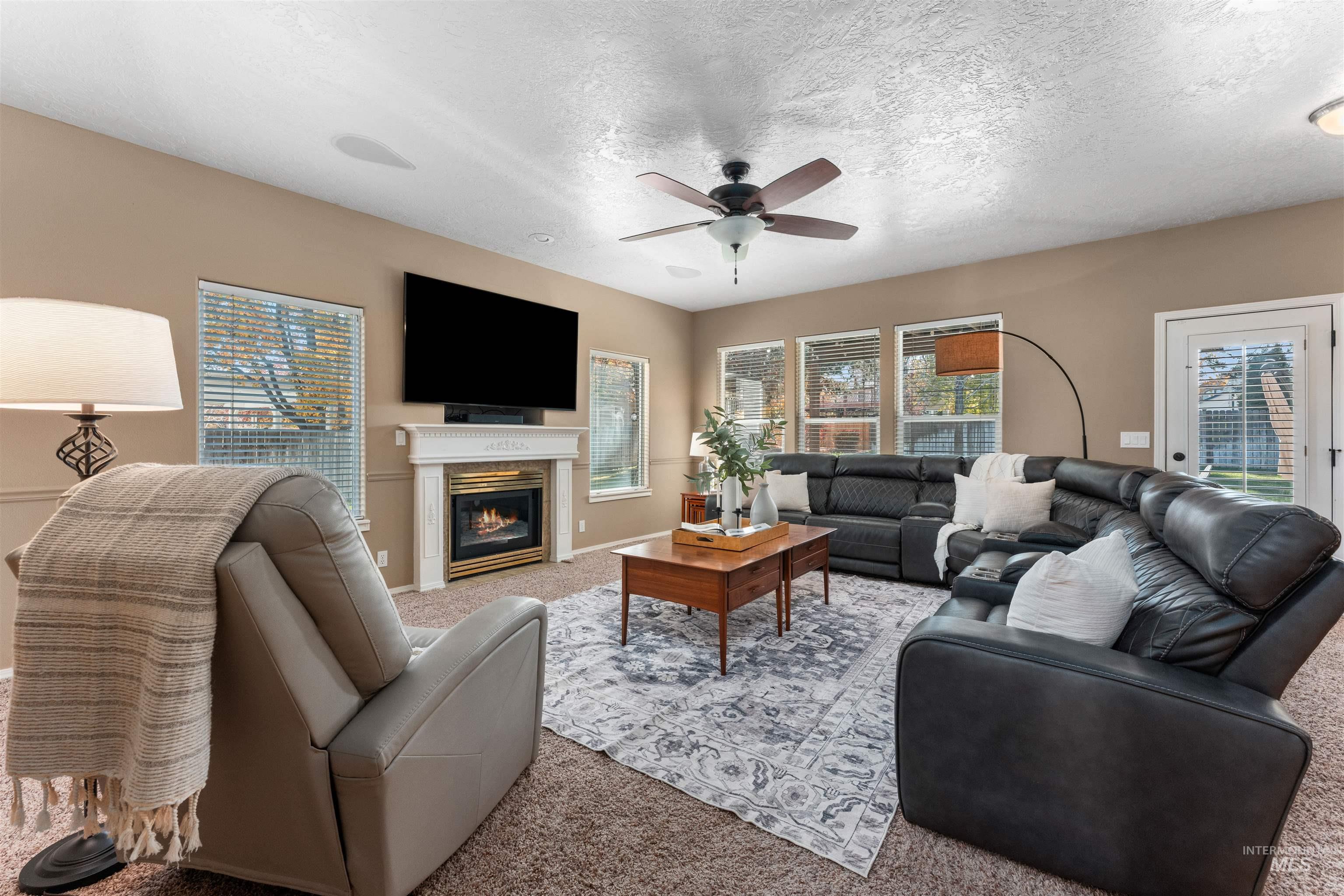 Carpeted living area featuring a textured ceiling, a glass covered fireplace, and a ceiling fan