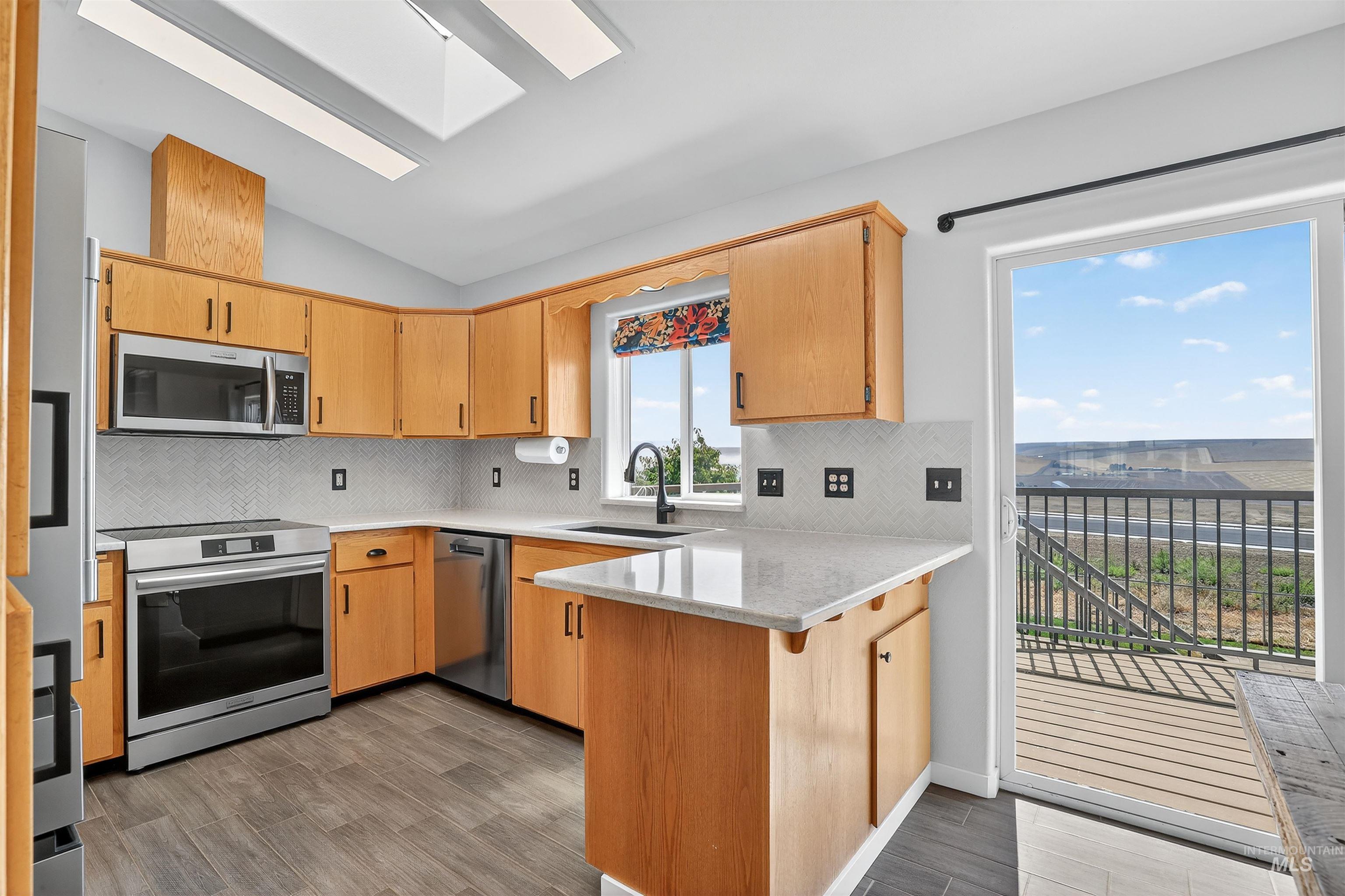 Kitchen featuring backsplash, a skylight, appliances with stainless steel finishes, dark wood-style flooring, and vaulted ceiling