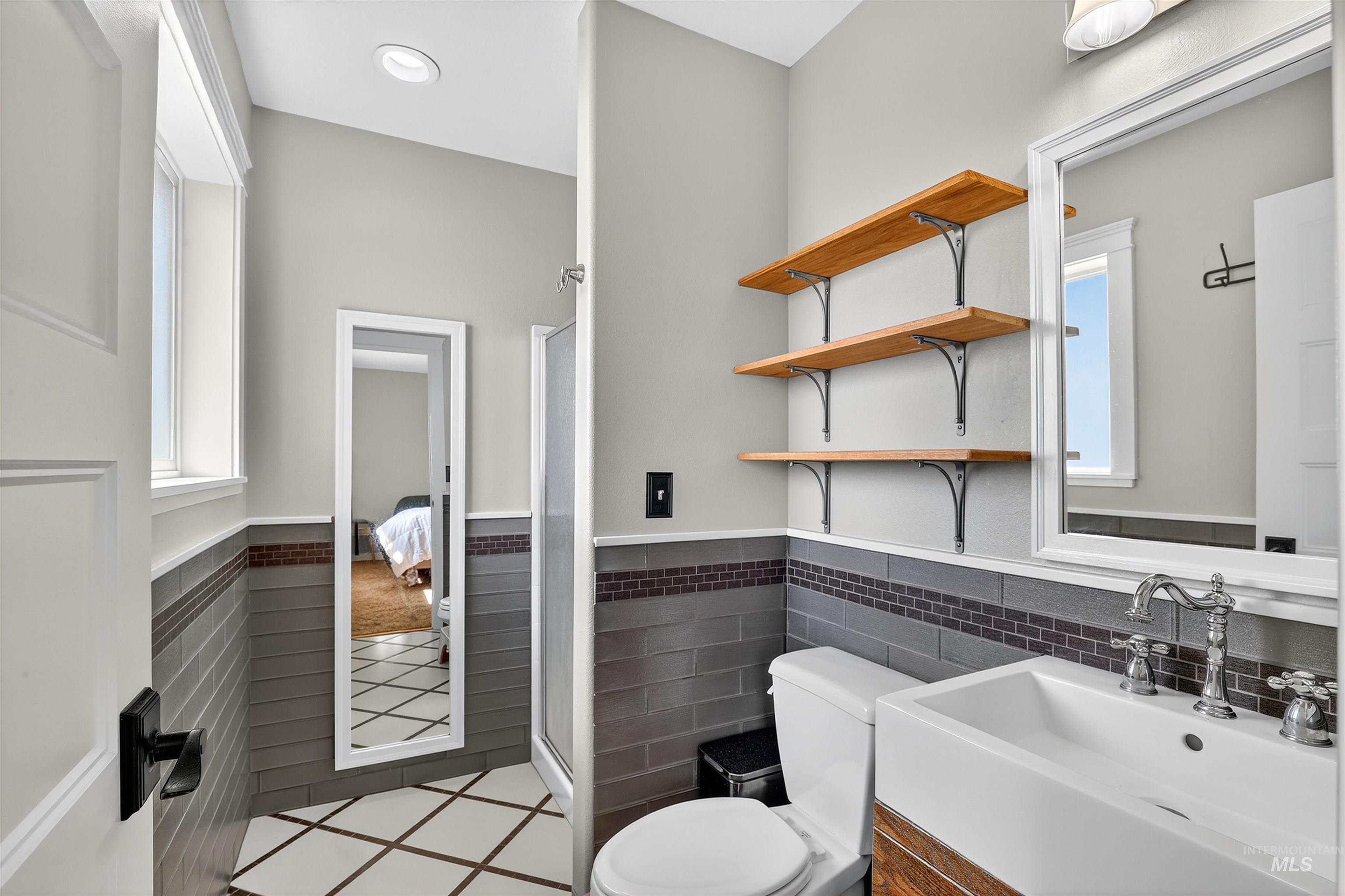 Full bathroom with healthy amount of natural light, a shower stall, vanity, a wainscoted wall, and light tile patterned flooring