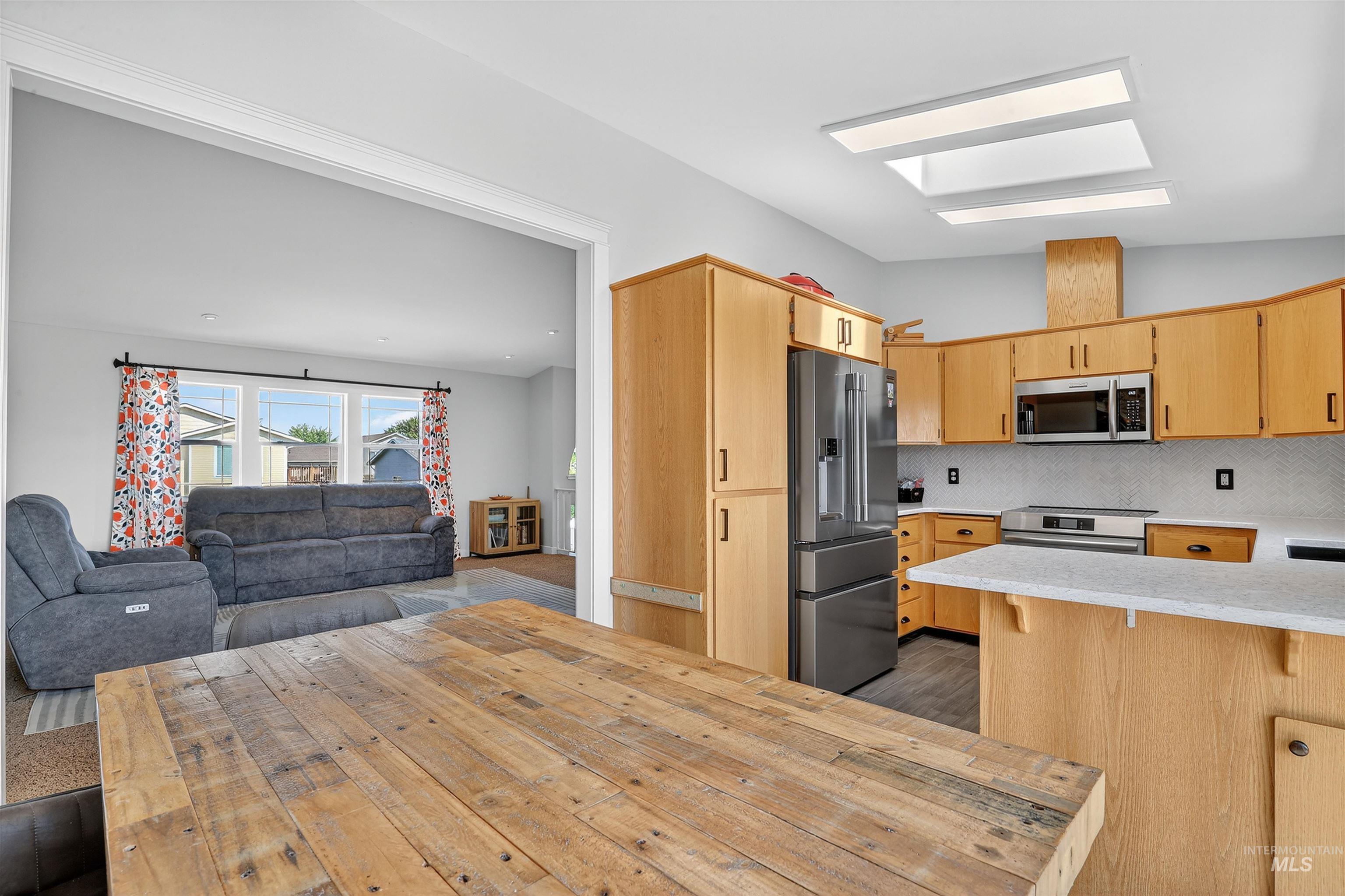 Kitchen with open floor plan, backsplash, appliances with stainless steel finishes, light brown cabinetry, and a kitchen breakfast bar
