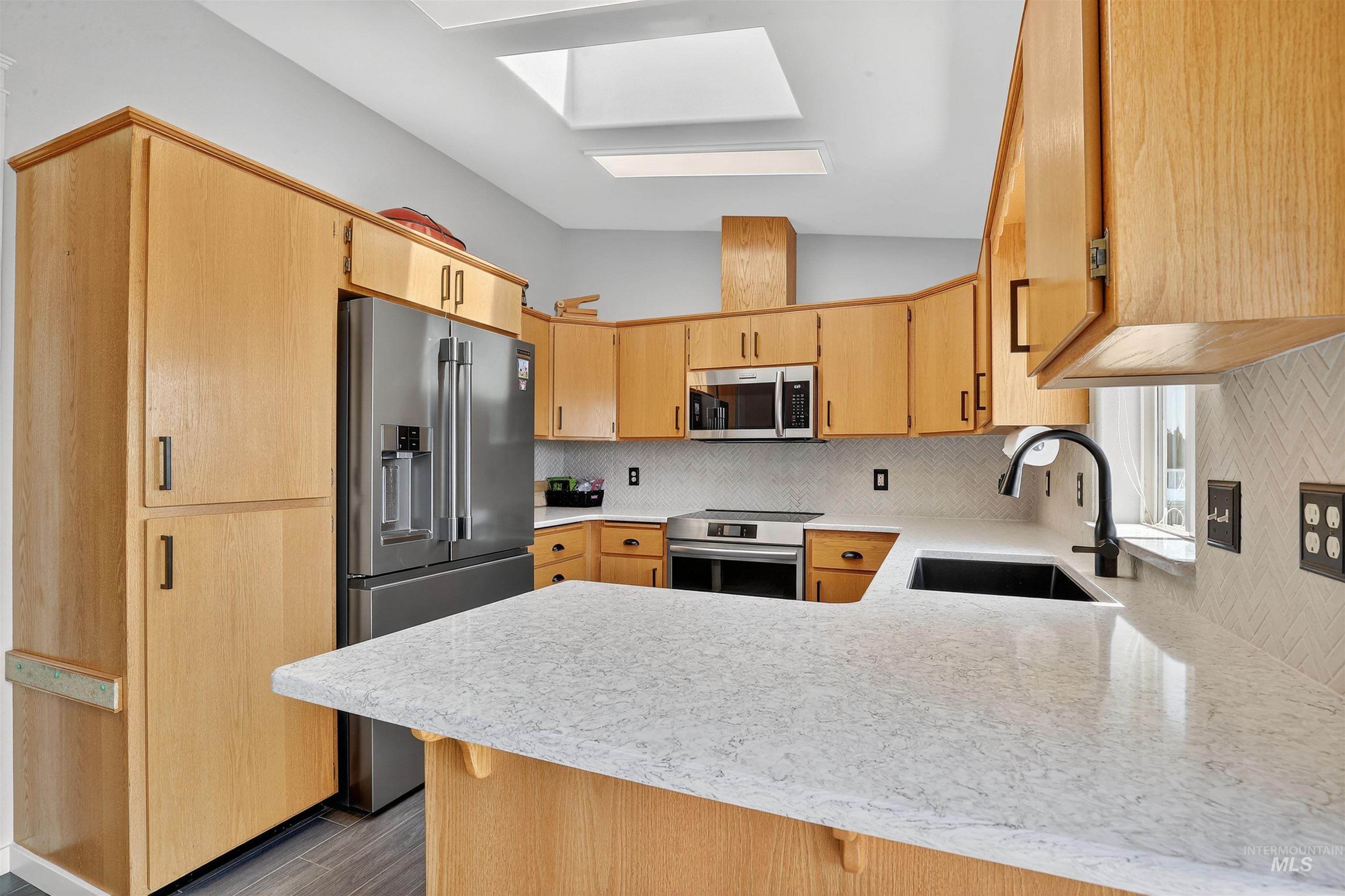 Kitchen featuring backsplash, a peninsula, stainless steel appliances, vaulted ceiling, and a skylight