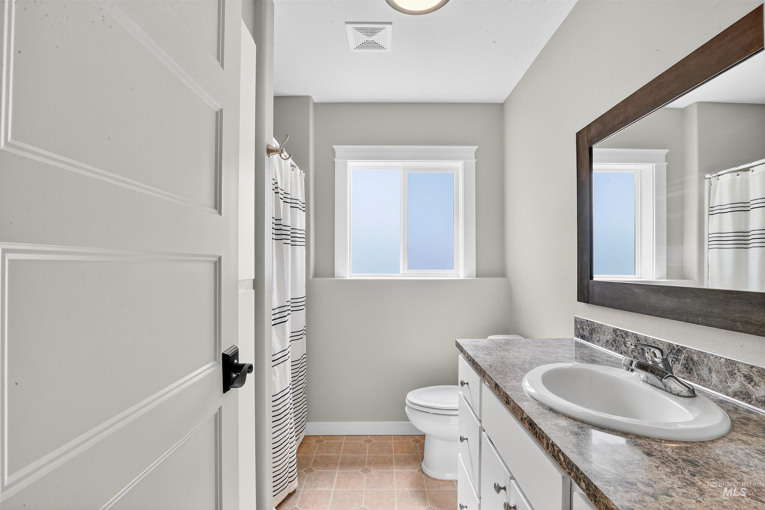 Full bathroom with vanity, light tile patterned floors, and curtained shower