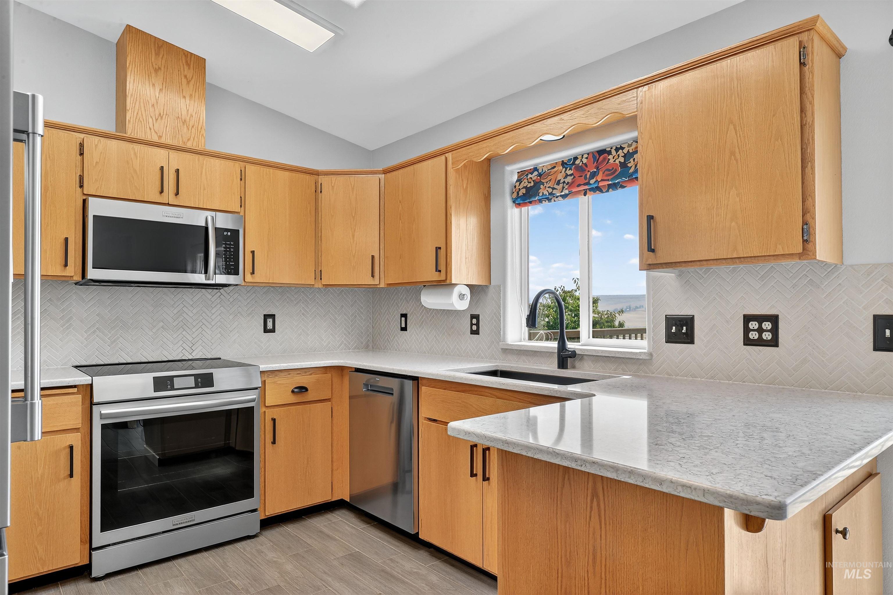 Kitchen with lofted ceiling, a peninsula, decorative backsplash, stainless steel appliances, and light stone countertops