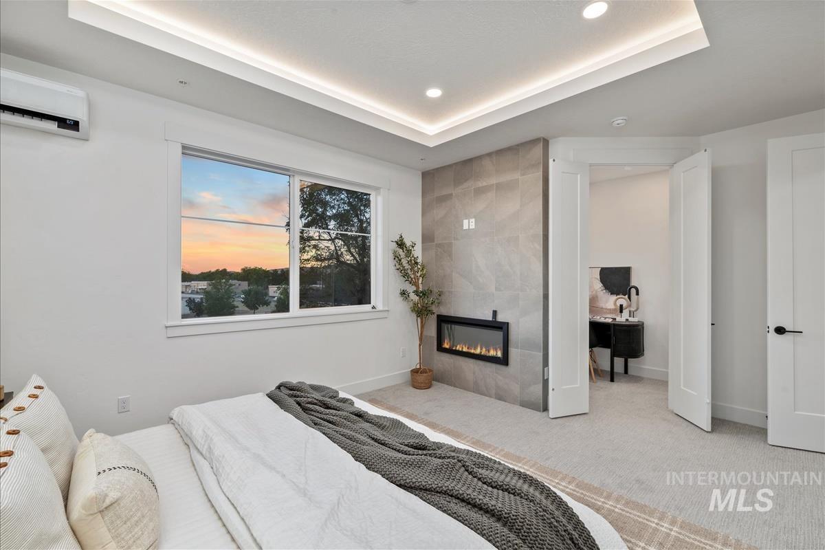 Bedroom featuring a tray ceiling, carpet flooring, a fireplace, a wall mounted air conditioner, and recessed lighting