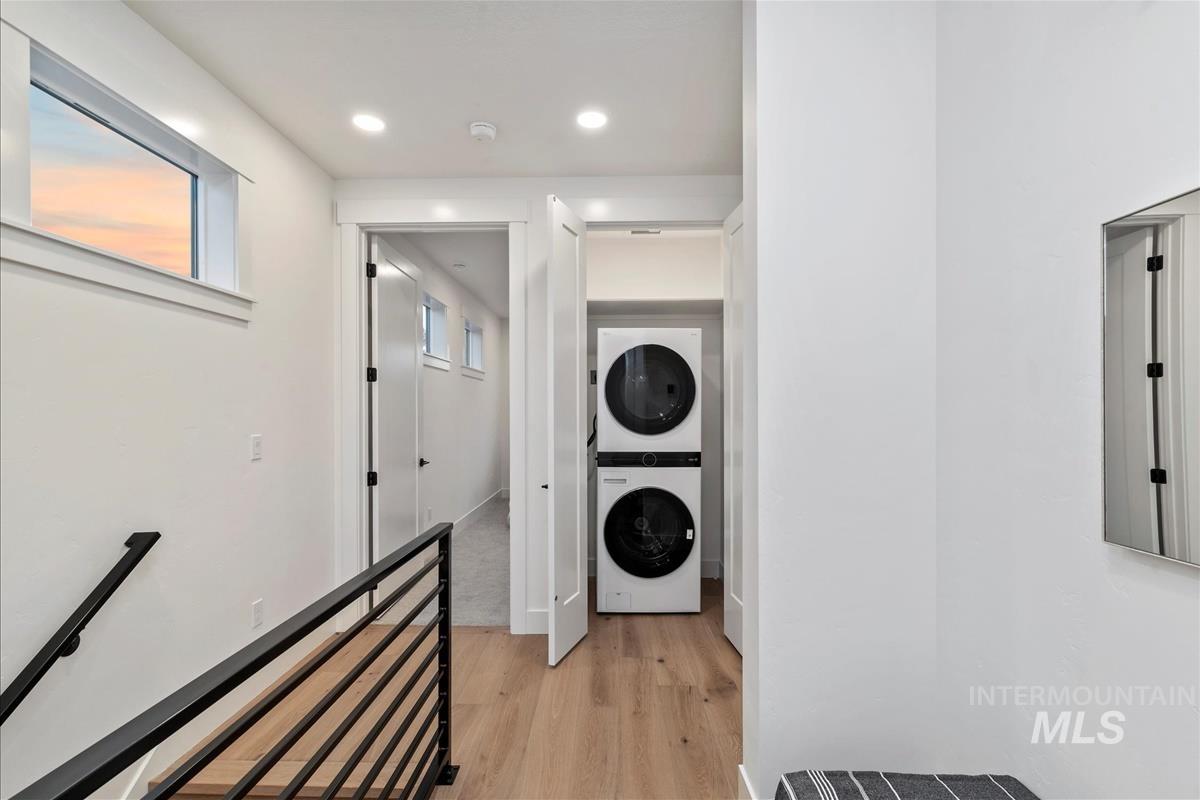 Laundry area featuring light wood-type flooring, stacked washer and clothes dryer, and recessed lighting