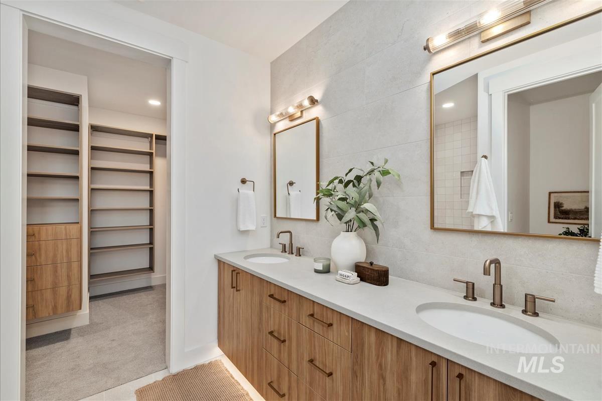 Bathroom with double vanity, a spacious closet, decorative backsplash, recessed lighting, and tile walls