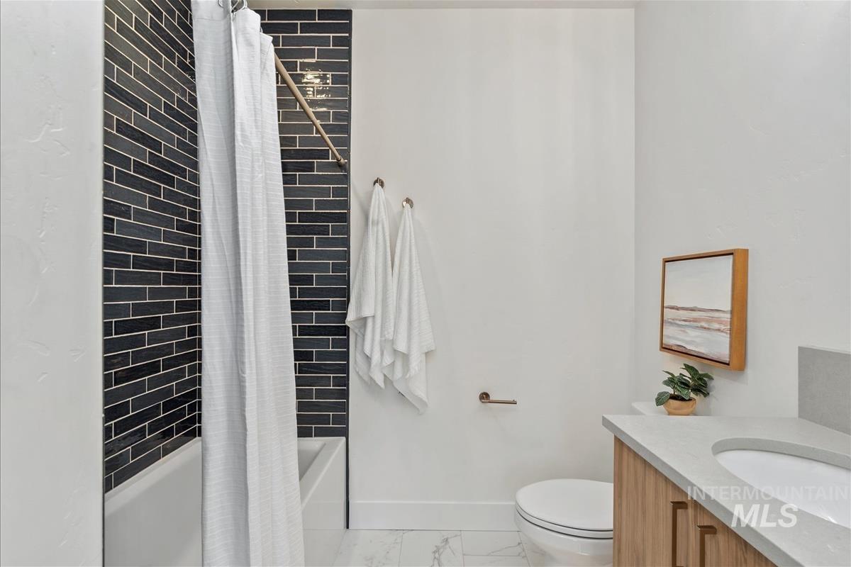 Bathroom with shower / bathtub combination with curtain, vanity, and light marble finish flooring