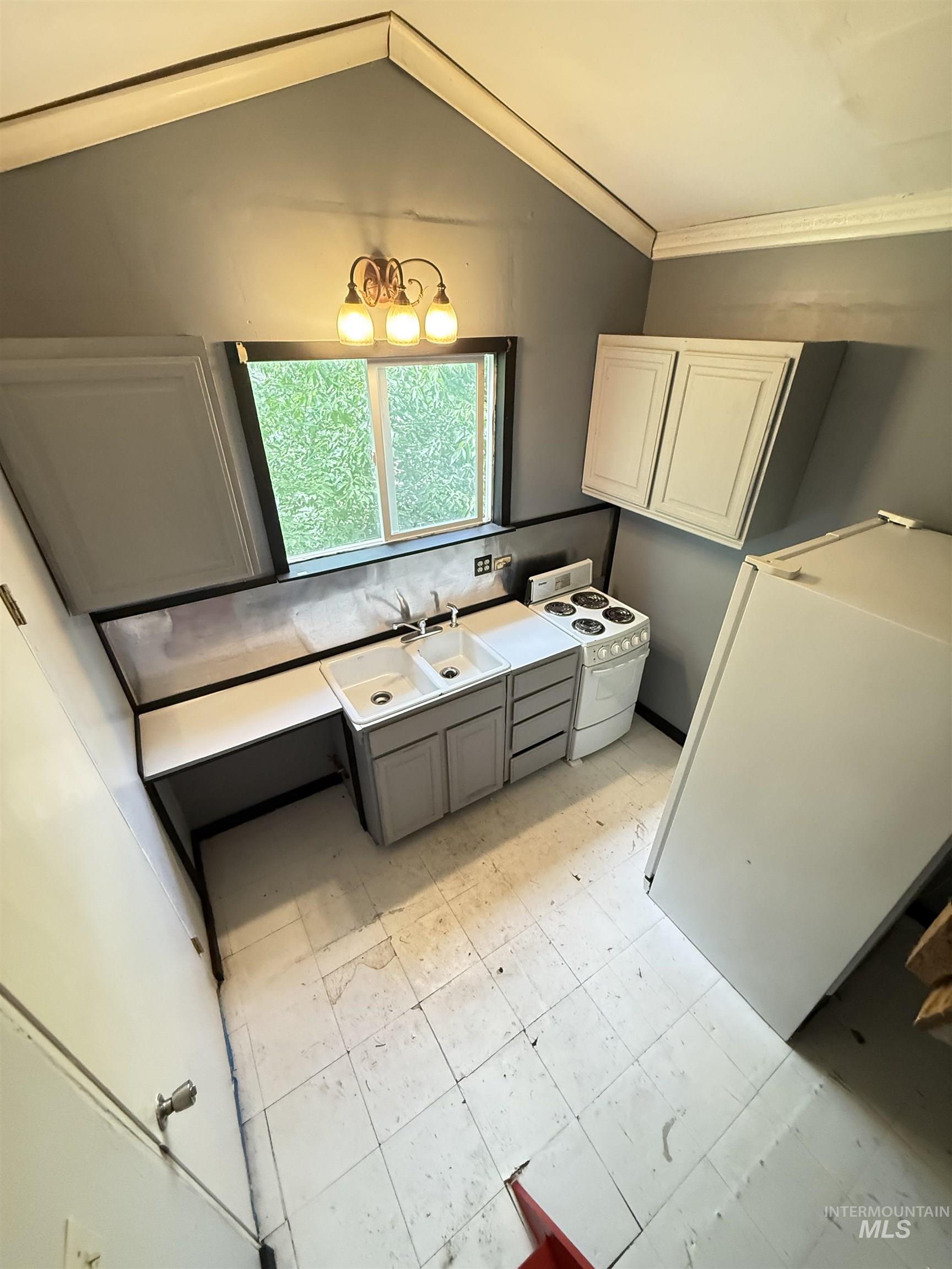 Kitchen featuring white appliances, lofted ceiling, crown molding, light floors, and backsplash