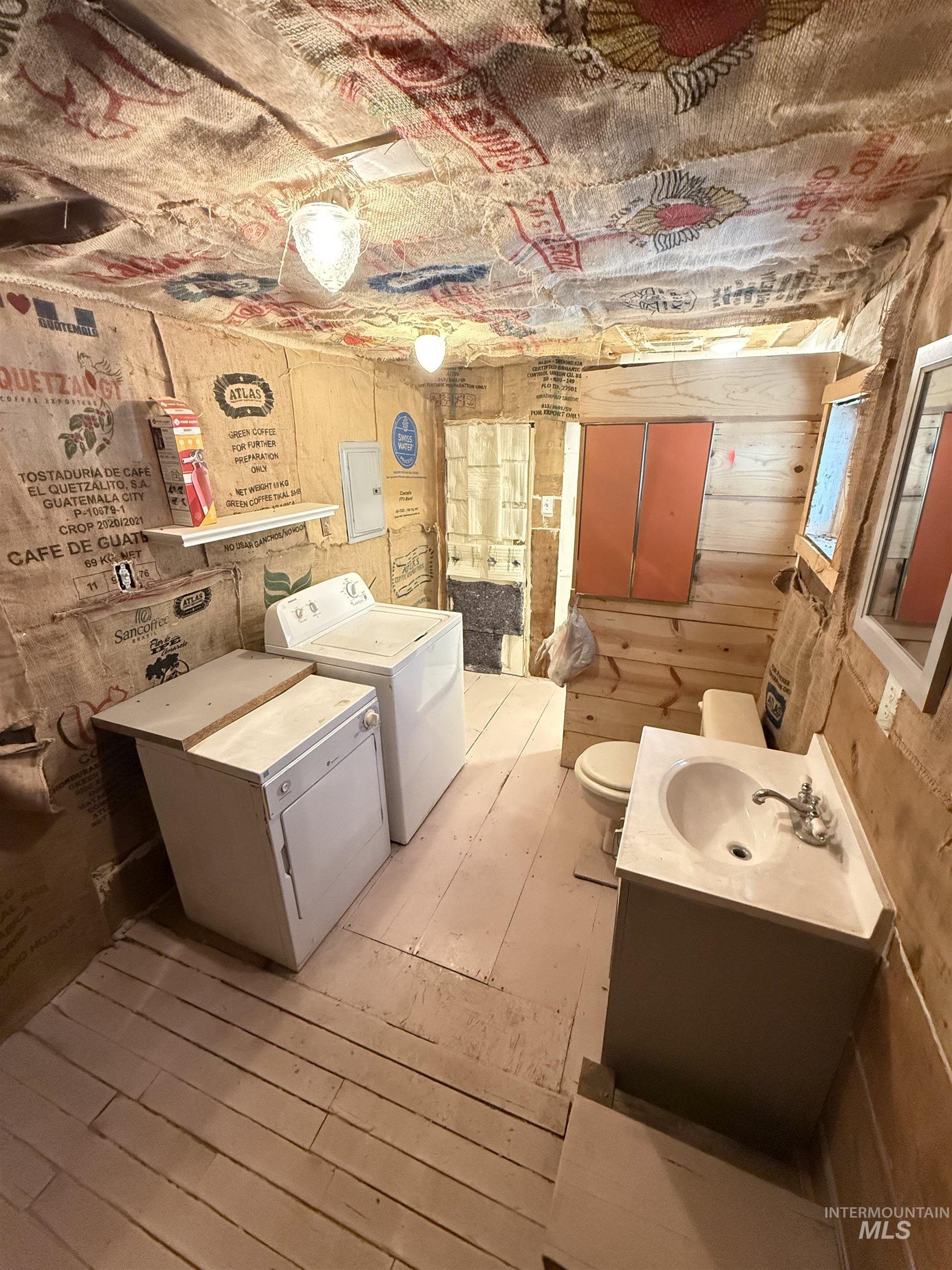 Washroom featuring separate washer and dryer, light wood-style floors, wooden walls, and electric panel