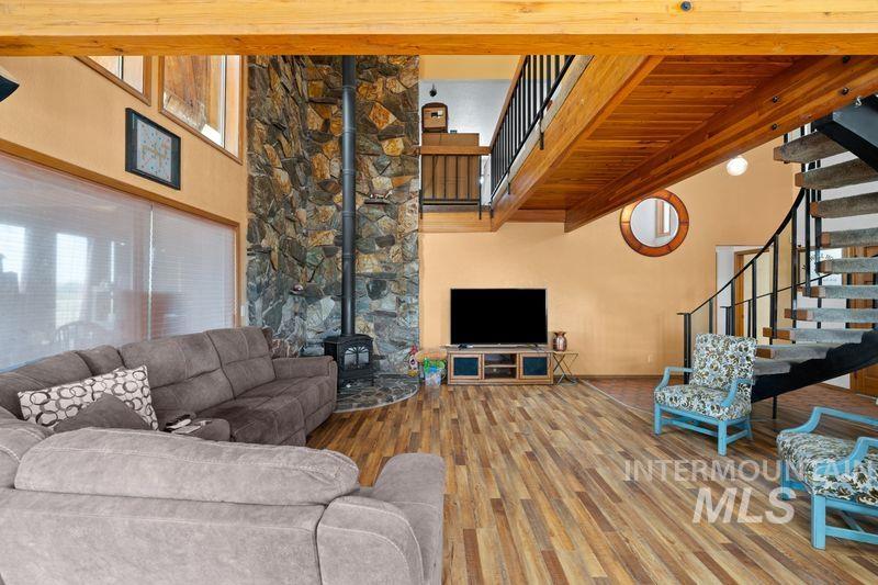 Living area with a wood stove, stairway, wood finished floors, a towering ceiling, and beam ceiling