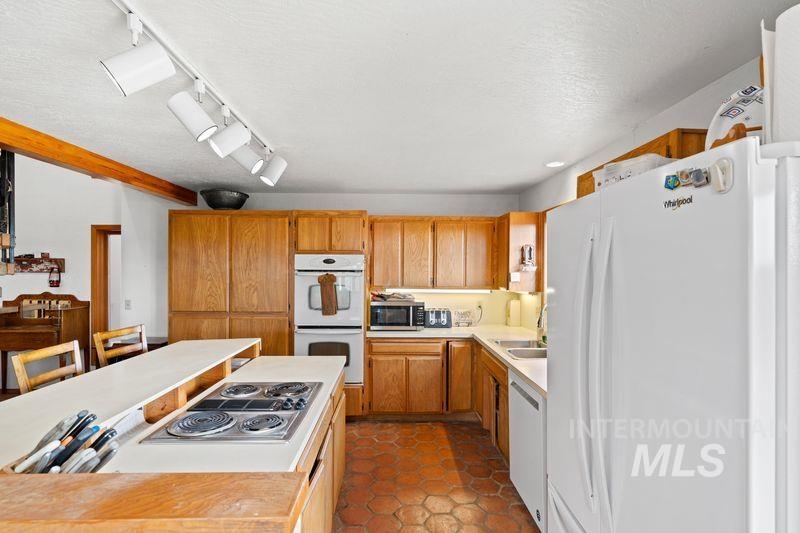 Kitchen featuring stainless steel appliances, light countertops, track lighting, a textured ceiling, and dark tile patterned flooring