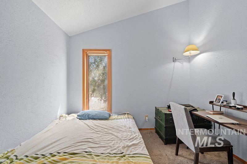 Bedroom with a textured wall, lofted ceiling, light carpet, a textured ceiling, and an office area