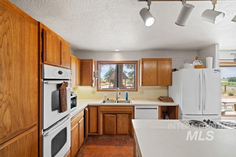 Kitchen with a textured ceiling, white appliances, light countertops, brown cabinets, and dark tile patterned flooring