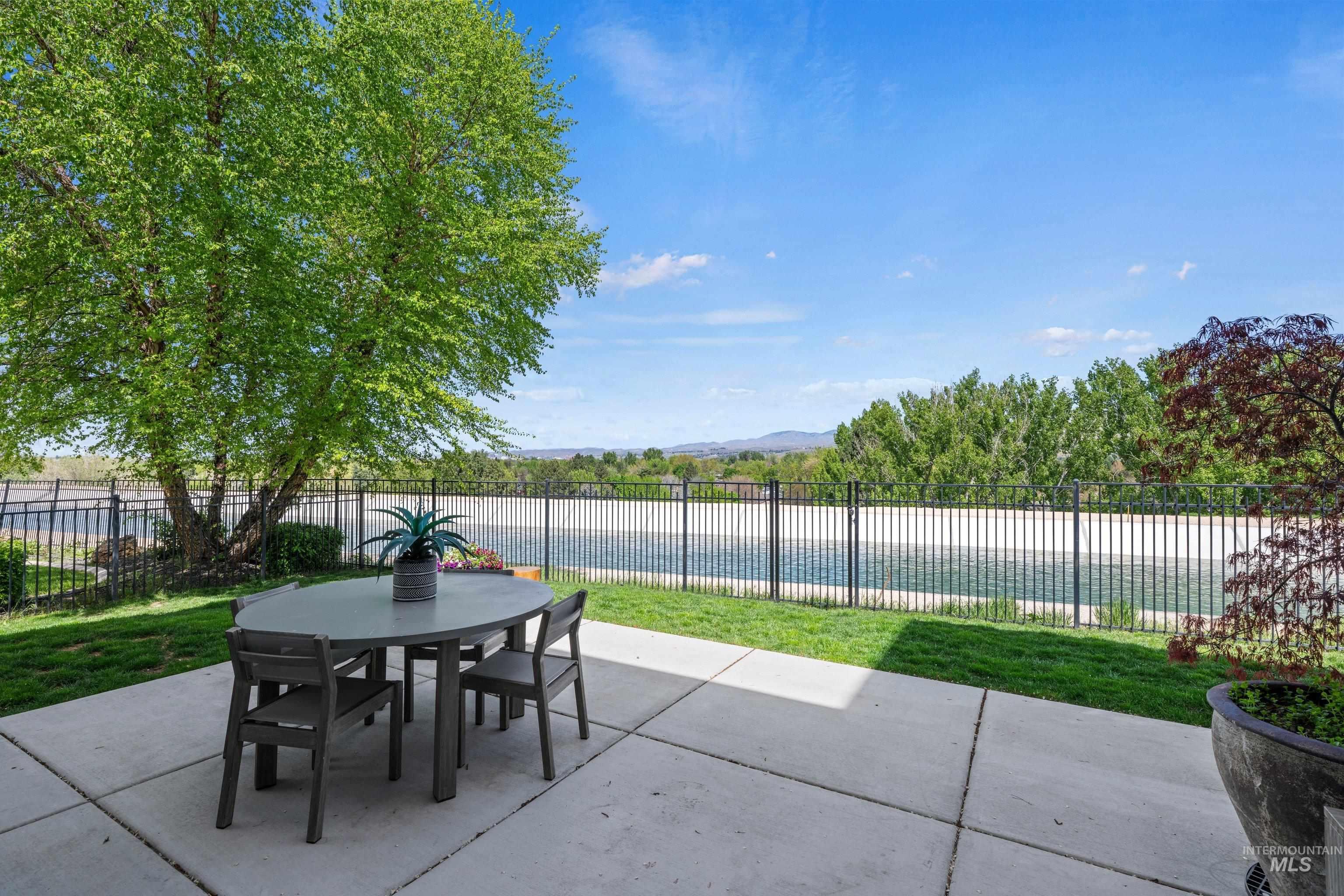 Concrete patio with expansive green lawn, black metal fencing, mature trees, and distant mountain scenery