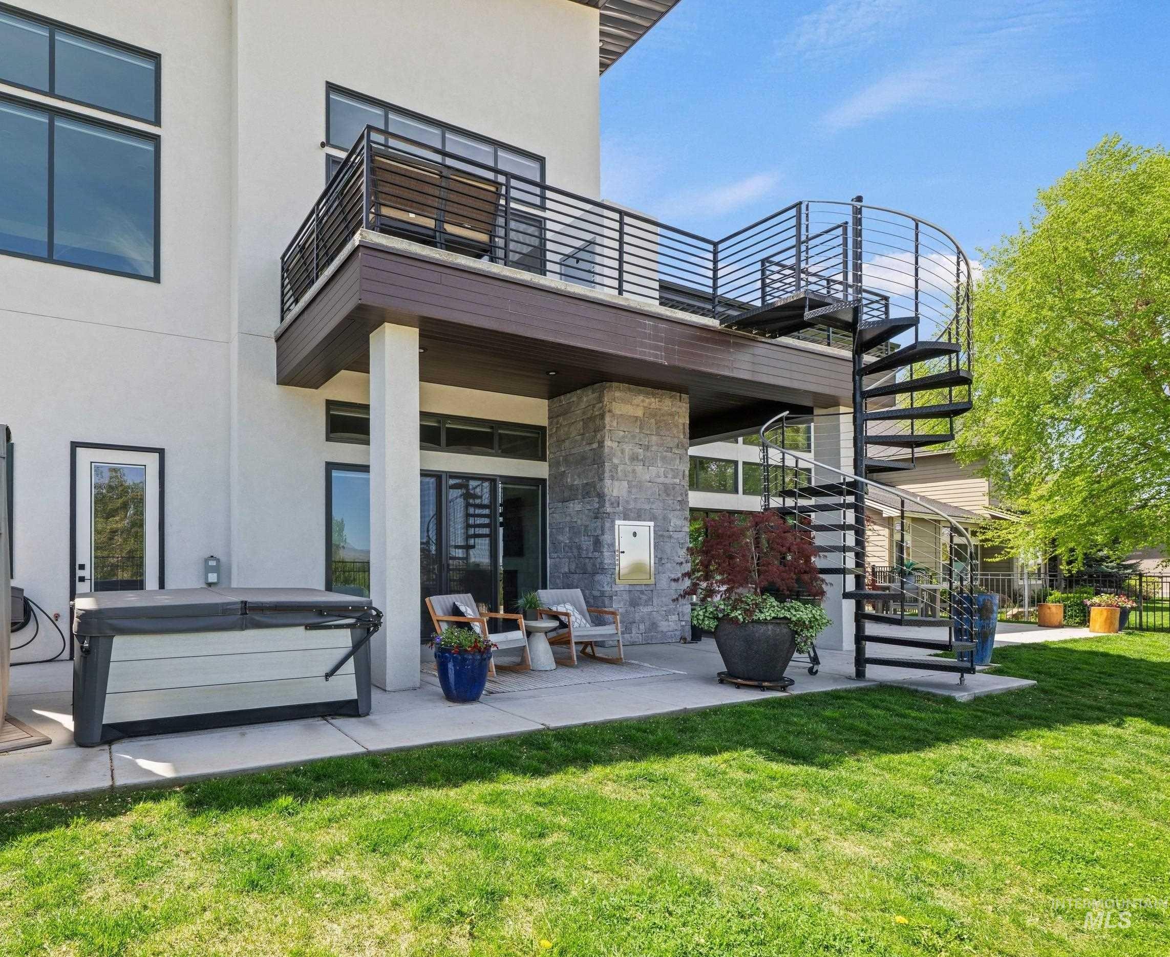 Expansive concrete patio featuring a modern spiral staircase, exterior balcony with railing, and a built-in outdoor grill