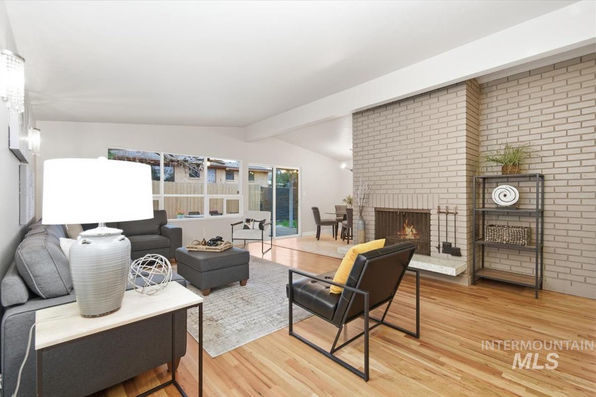 Living room with light wood-style floors, a fireplace, and lofted ceiling with beams