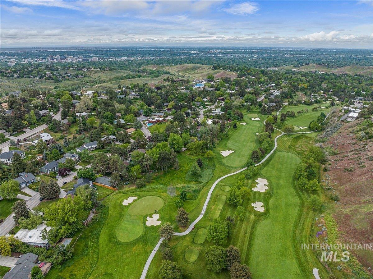 Aerial view of property and surrounding area featuring a golf course and nearby suburban area