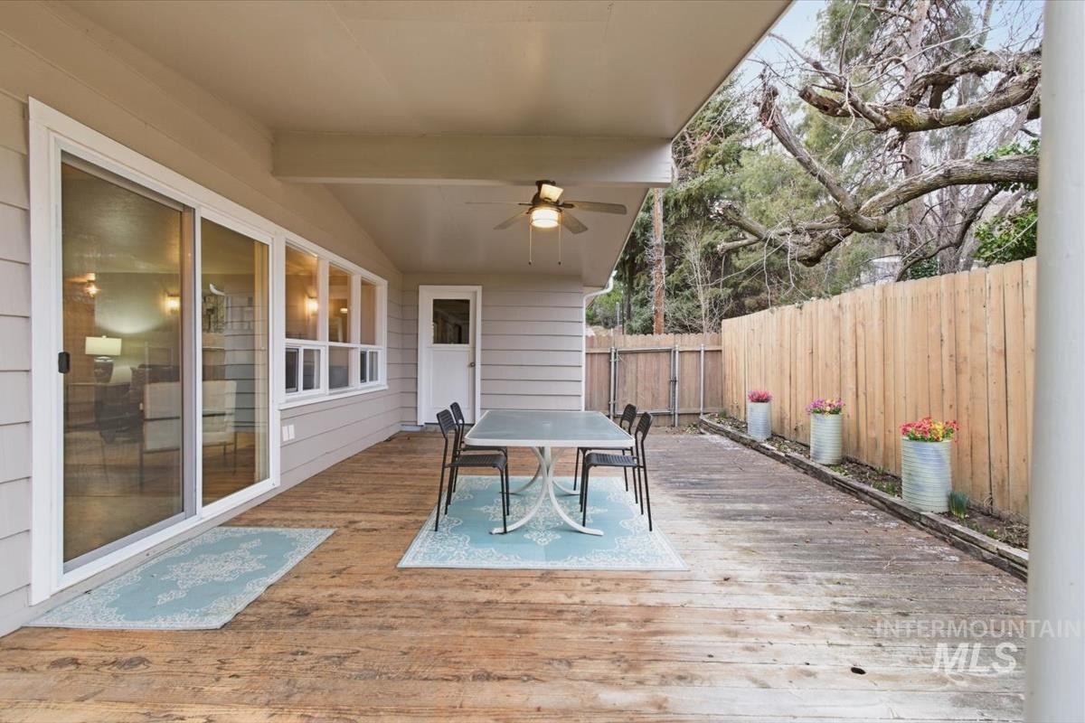 Wooden terrace featuring outdoor dining space, a ceiling fan, and a fenced backyard