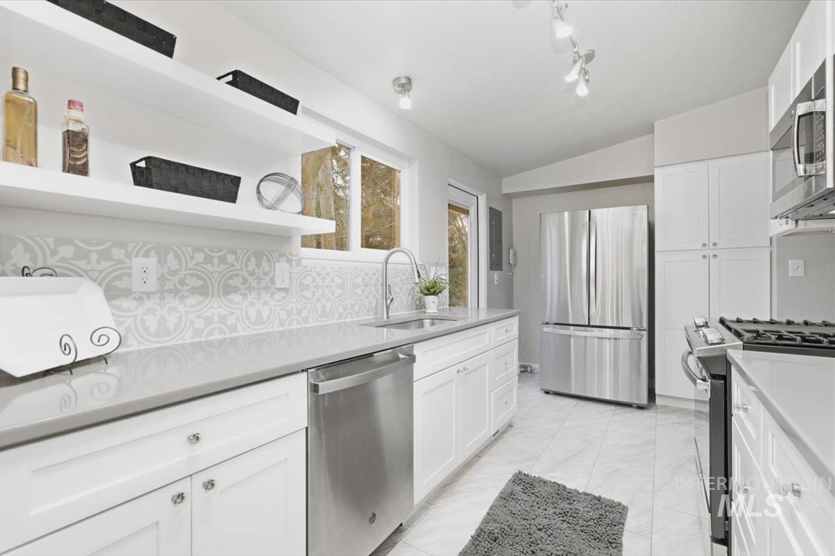 Kitchen with open shelves, stainless steel appliances, white cabinets, vaulted ceiling, and backsplash