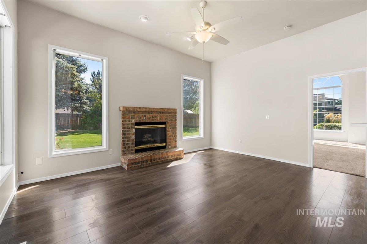 Unfurnished living room with ceiling fan, a fireplace, dark wood finished floors, and plenty of natural light