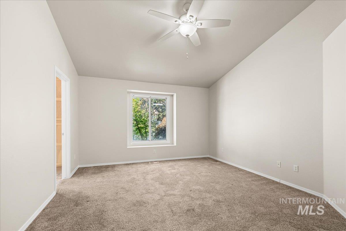 Spare room featuring light colored carpet, lofted ceiling, and a ceiling fan