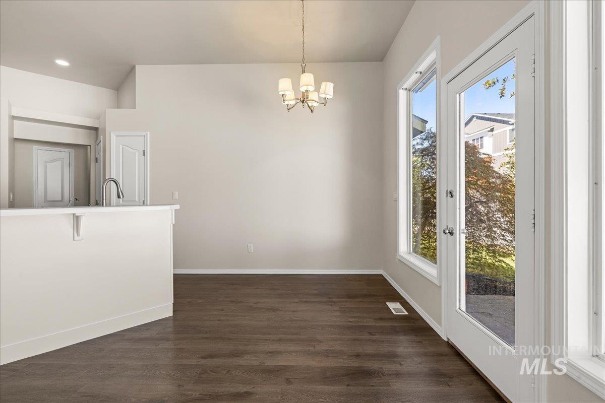 Unfurnished dining area with healthy amount of natural light, dark wood-type flooring, and a chandelier