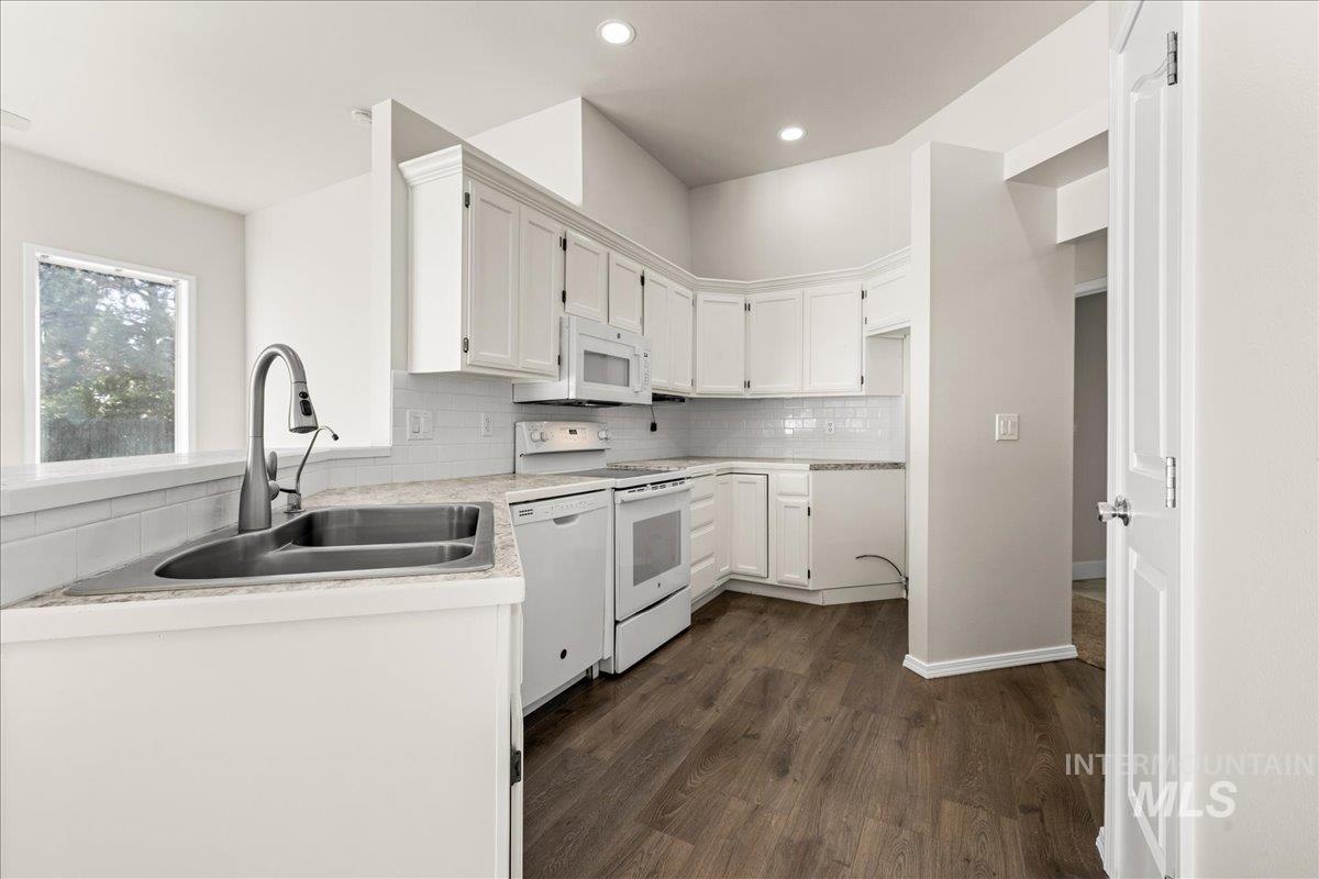 Kitchen featuring white appliances, backsplash, dark wood-style floors, white cabinets, and recessed lighting