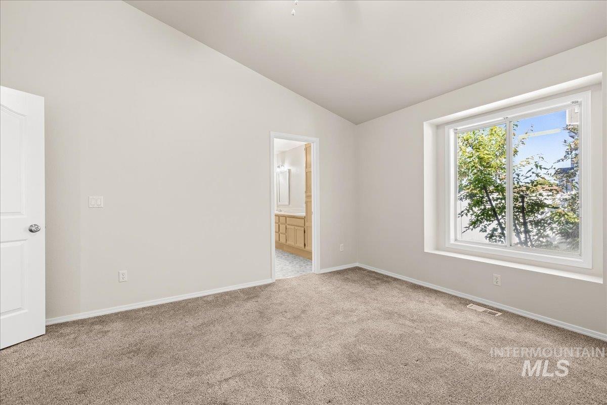 Unfurnished bedroom with vaulted ceiling, light carpet, and ensuite bath
