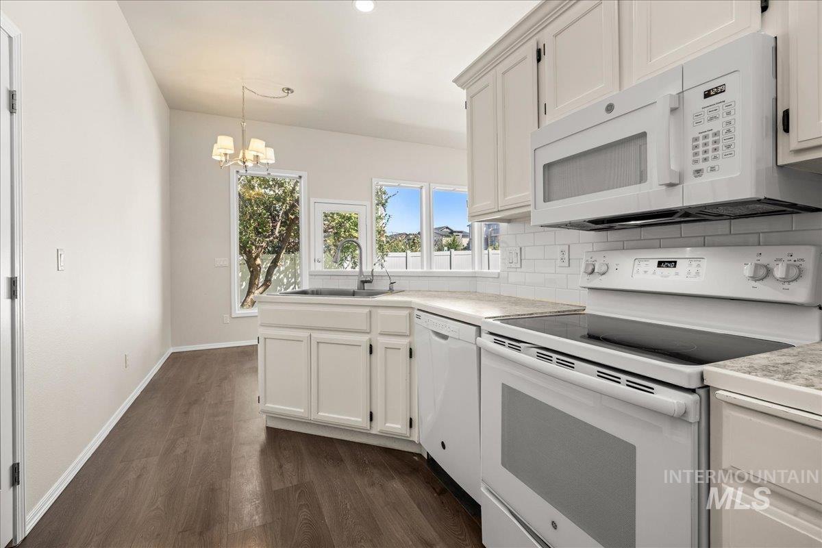 Kitchen featuring white appliances, dark wood-type flooring, backsplash, a chandelier, and white cabinetry