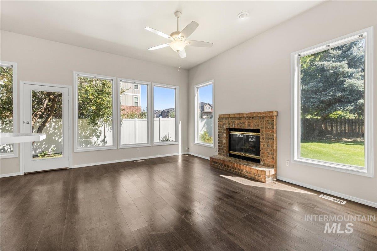 Unfurnished living room with a brick fireplace, dark wood-style flooring, and ceiling fan