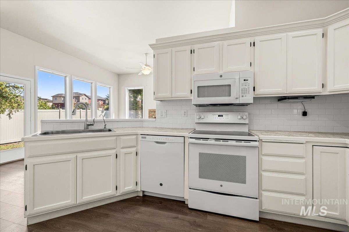 Kitchen with white appliances, light countertops, white cabinetry, and backsplash