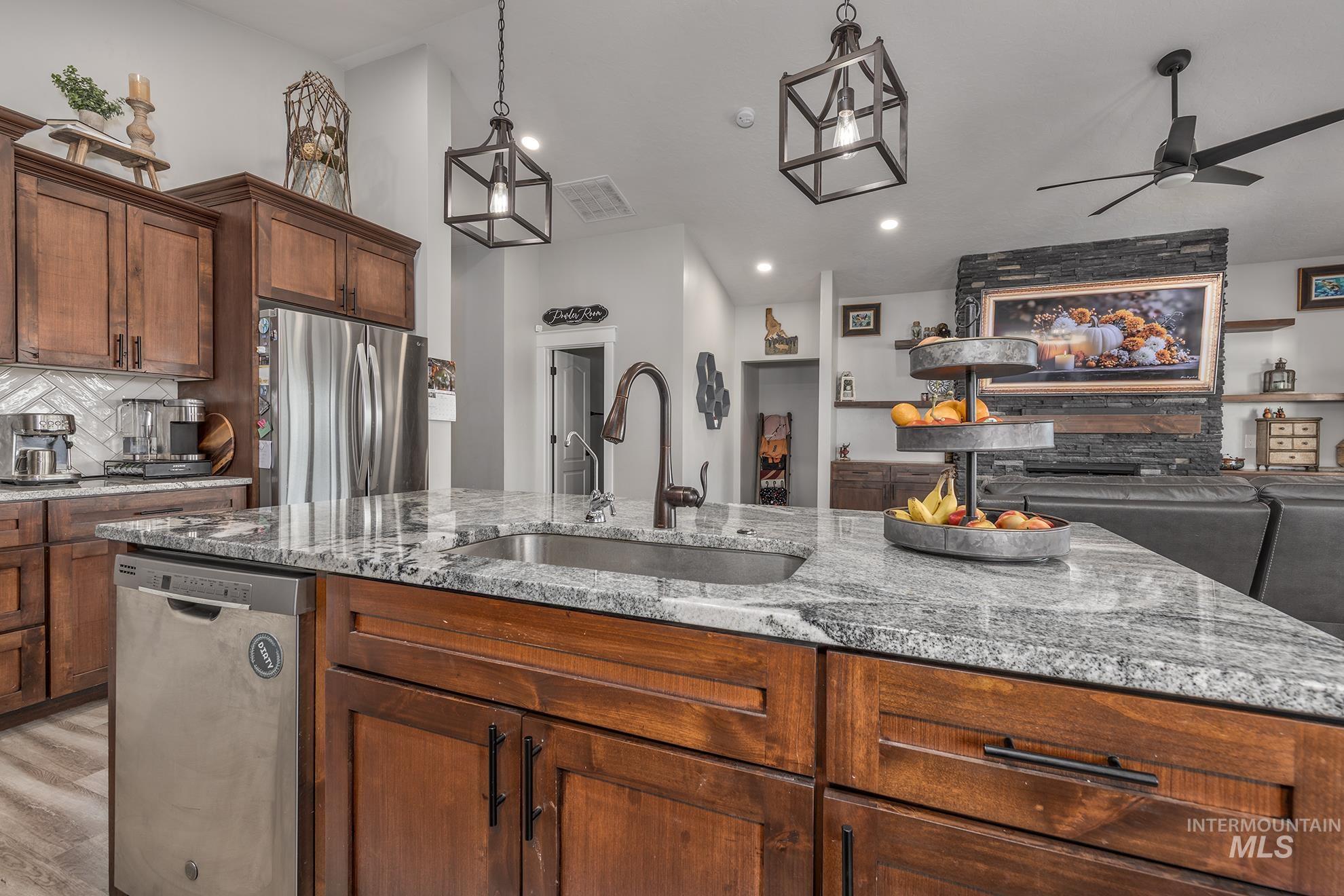 Kitchen with tasteful backsplash, appliances with stainless steel finishes, pendant lighting, light stone counters, and open floor plan